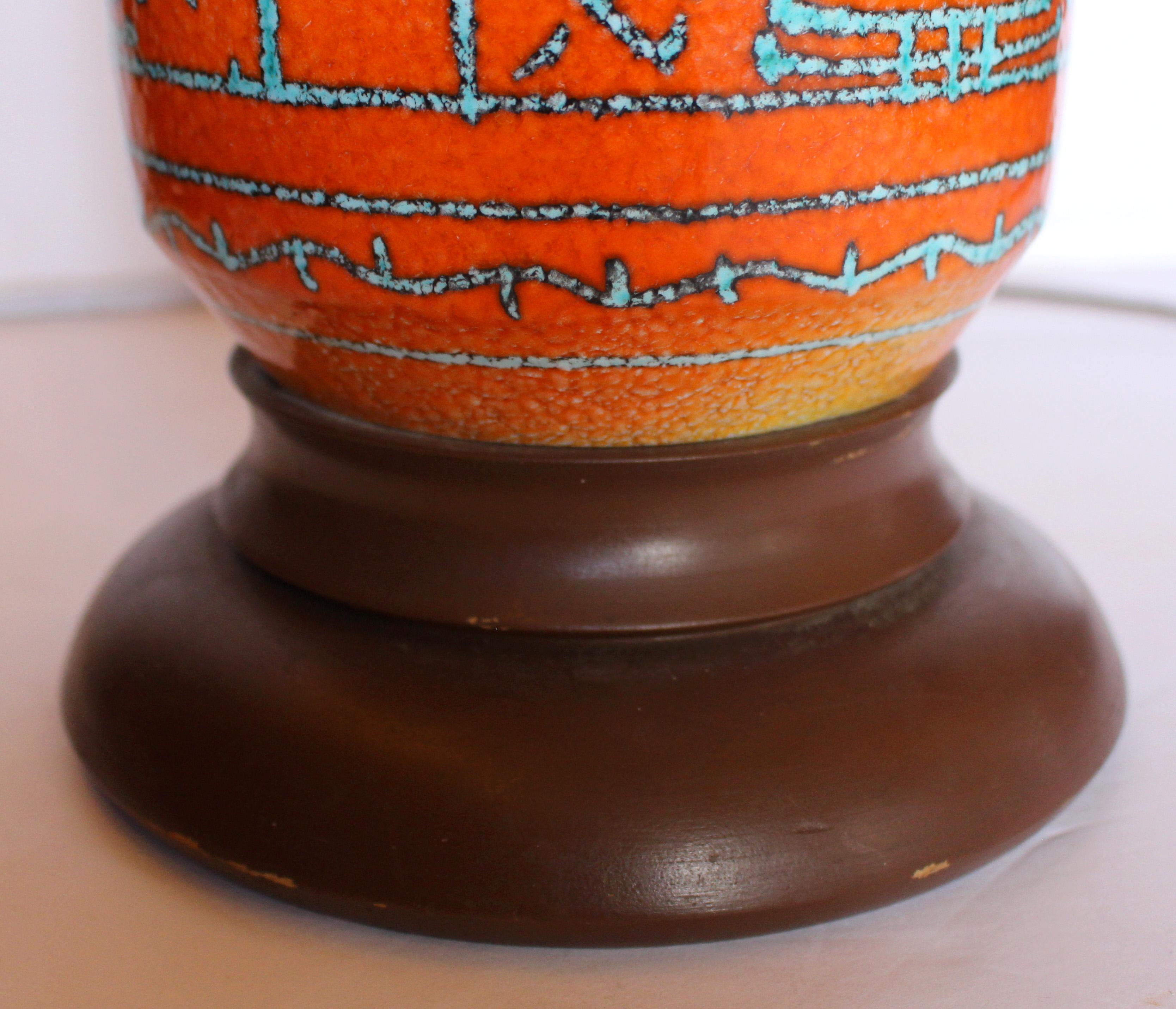 Circa 1950-60s mid century modern ceramic lamp. Forme cylindrique exceptionnellement audacieuse avec col incliné. L'orange doux-amer contraste avec les motifs géométriques turquoise. Base en bois tourné. 37