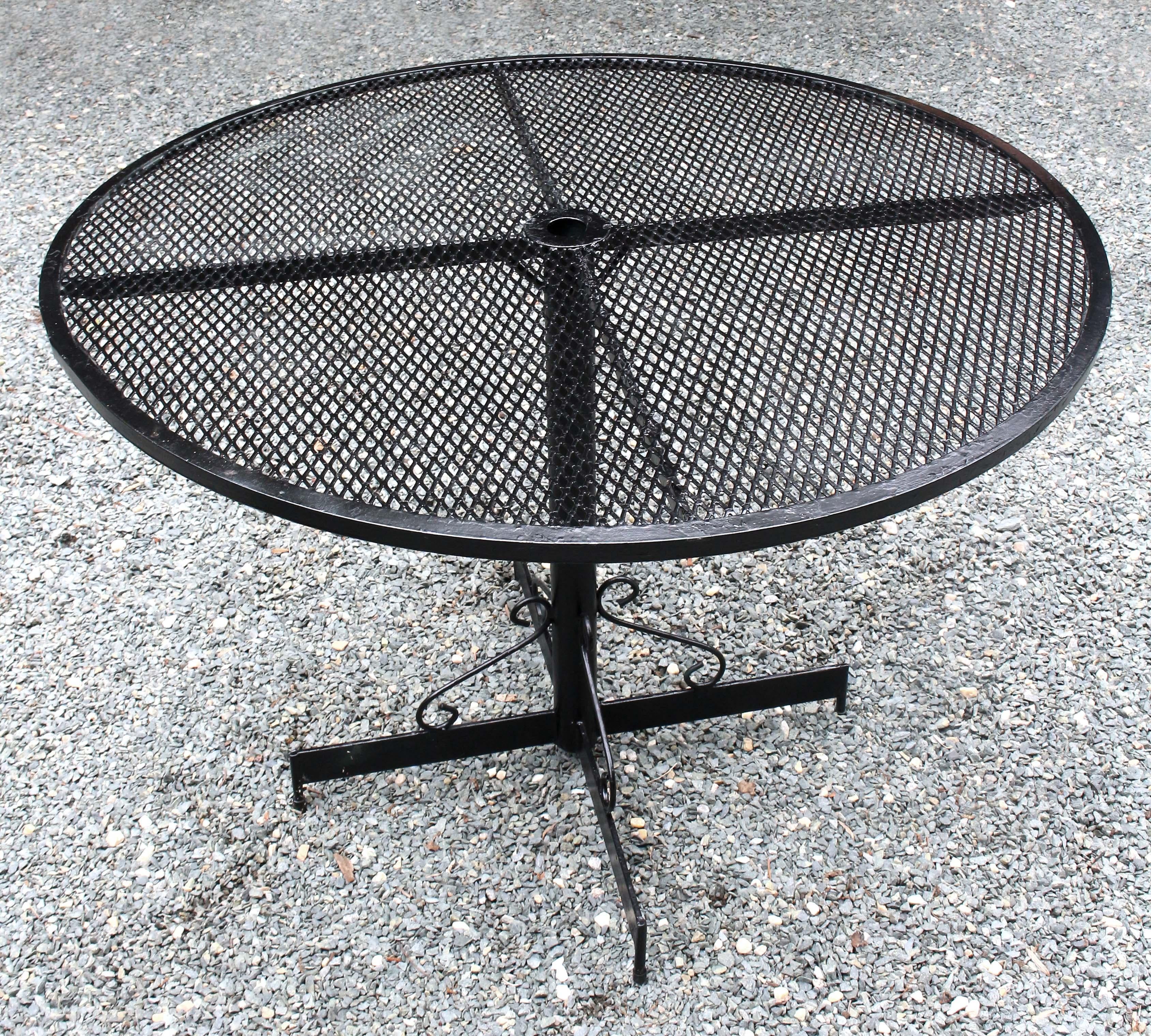 Circa 1950-70 wrought iron outdoor table & four arm chairs. Attributed to Salterini. Comfortable rounded backs & scrolled arms; the scroll picked up in the front leg decoration. Iron mesh seat & back. Note the rear legs which point down, rather then