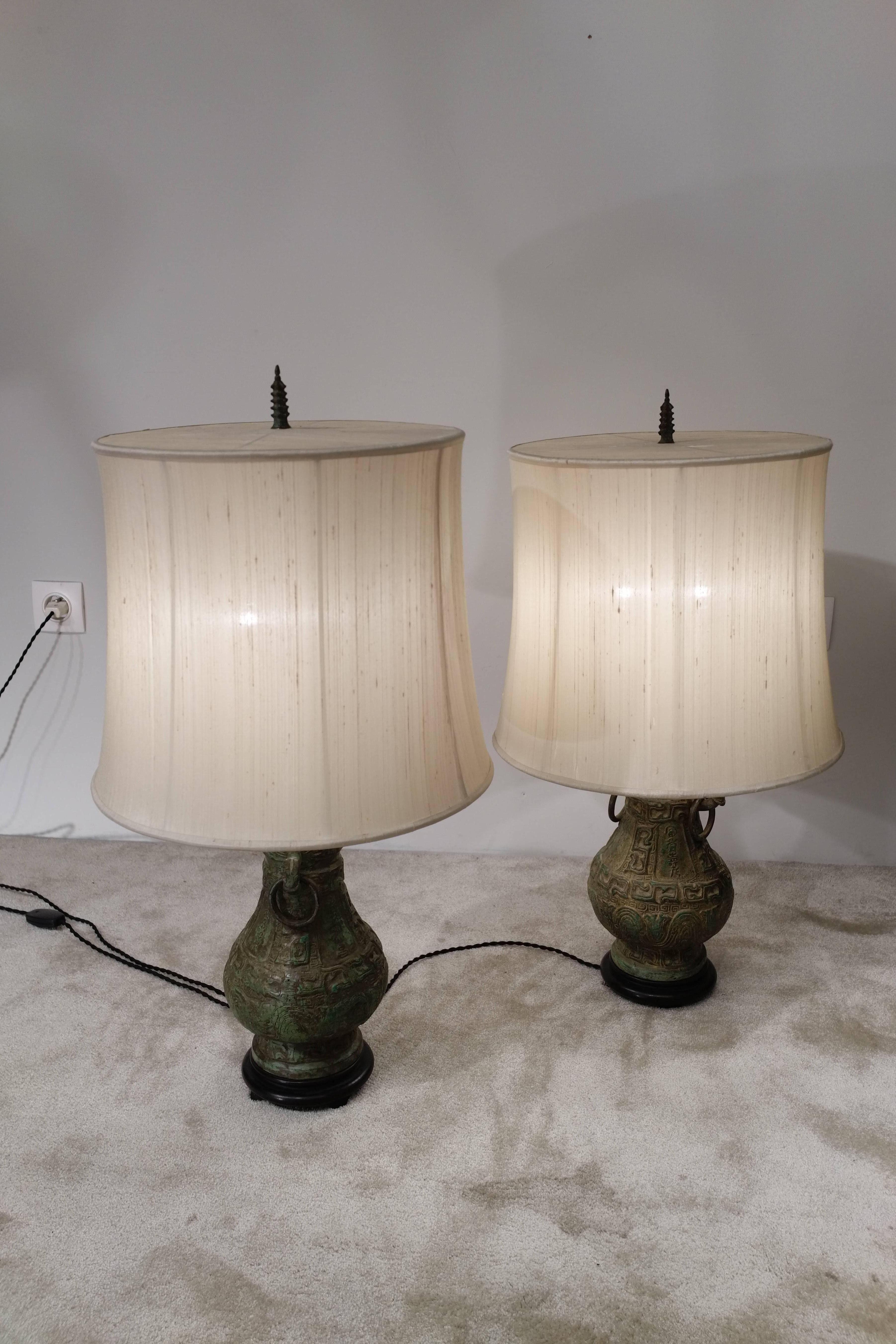 Pair of patinated bronze lamps in the Chinese style with original lampshades, circa 1950.
Two bulbs. Pagoda top liked. Black wood base.
Vintage fabrics (used and slighly stained). Re-electrified.

Dimensions: 
Height (with lampshades): 76cm /