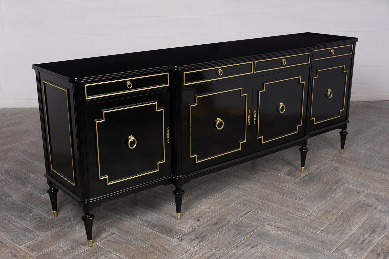 This 1950s Regency style buffet is made of mahogany wood stained in deep black color with a lacquered finish. The wood top features a carved edge, four top drawers with gilt molding accents and decorative pulls. The cabinet doors have symmetrical