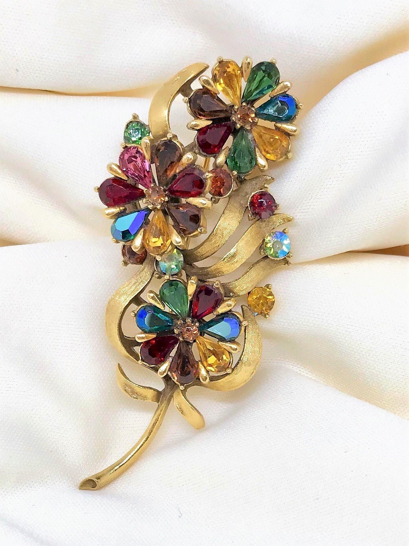 Circa 1960s Coro brooch in a floral and leaf motif done in a rich gold-tone brushed metal.  It is set with faceted glass pear-shape stones in multiple jewel-tone colors.  The brooch measures 3.25