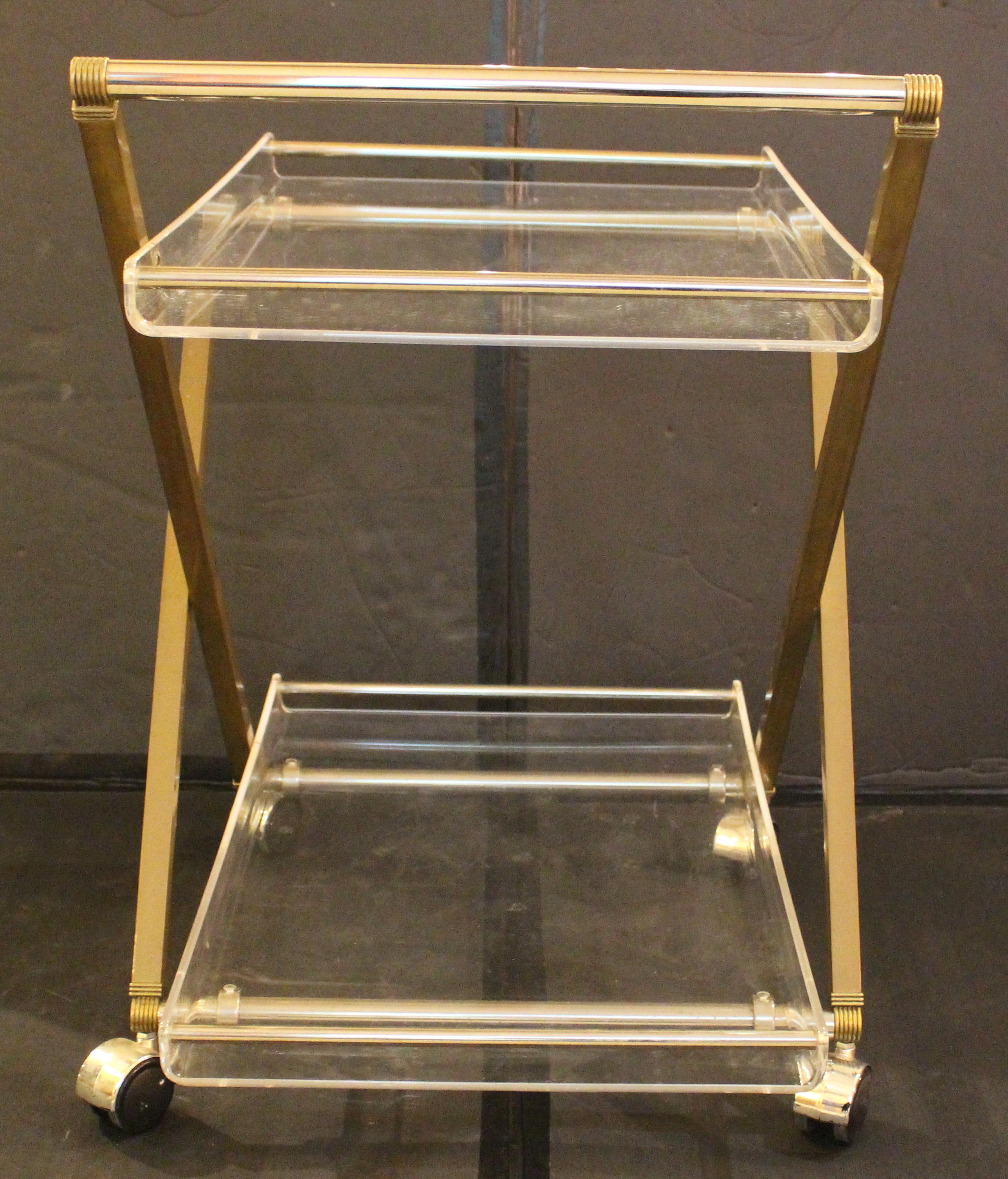 Circa 1960s lucite, chrome, and brass rolling bar cart, English. Mid century modern. X-form sides. Reeded details. Integral trays. Good overall condition commensurate with age and use. 19.8