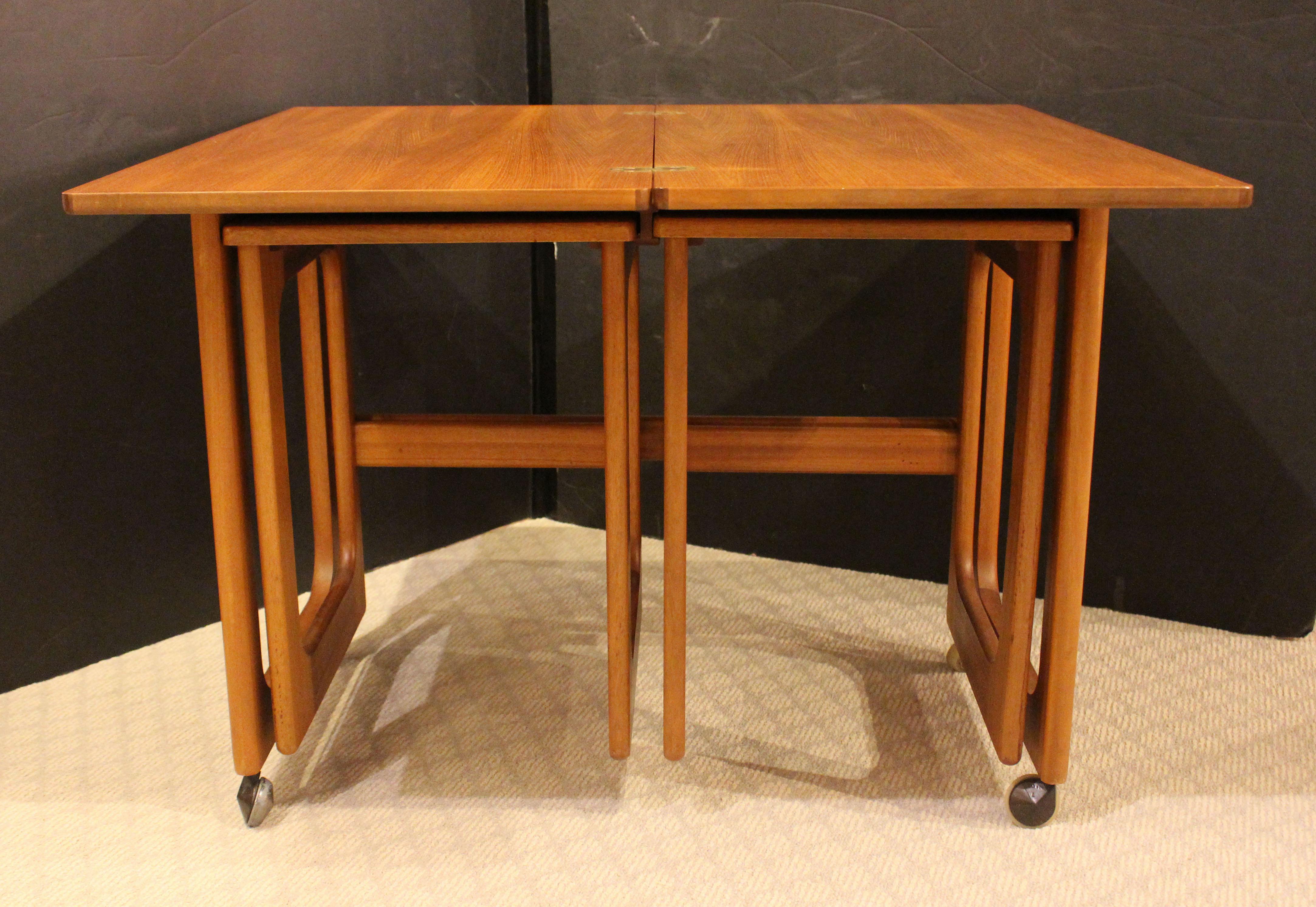 A set of Mid Century Modern teak tables, English, circa 1960s. A rotating flip top coffee table with two nesting tables hung underneath. By McIntosh. Minor ring stains to one nesting table.
Coffee table: 16