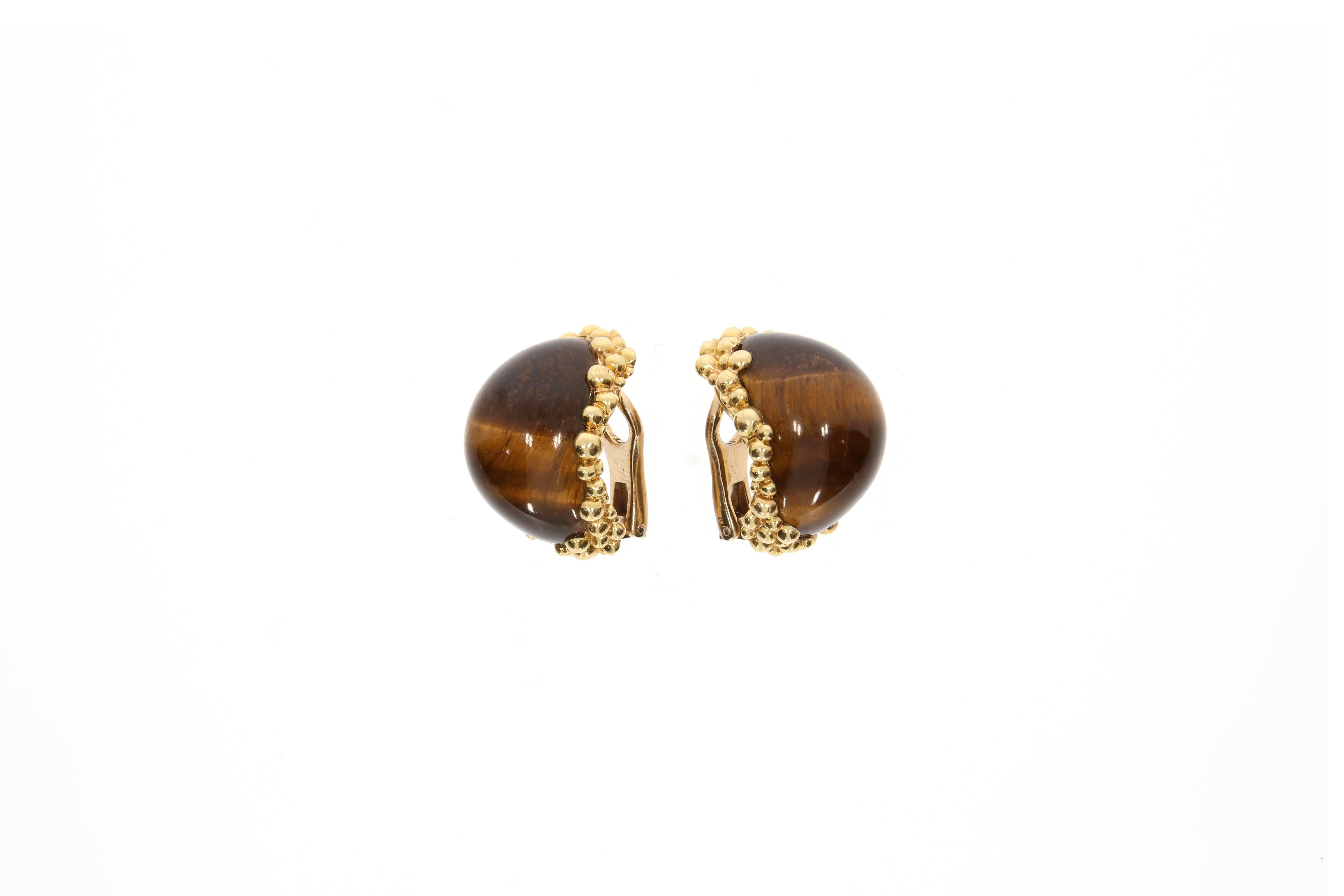 A pair of English 18 karat yellow gold and tiger´s eye ear clips, by Kutchinsky. Circa 1970´s. The cabochon- cut golden- brown shimmering stones are embedded in an 18 karat yellow gold refined and artistic setting. Signed 