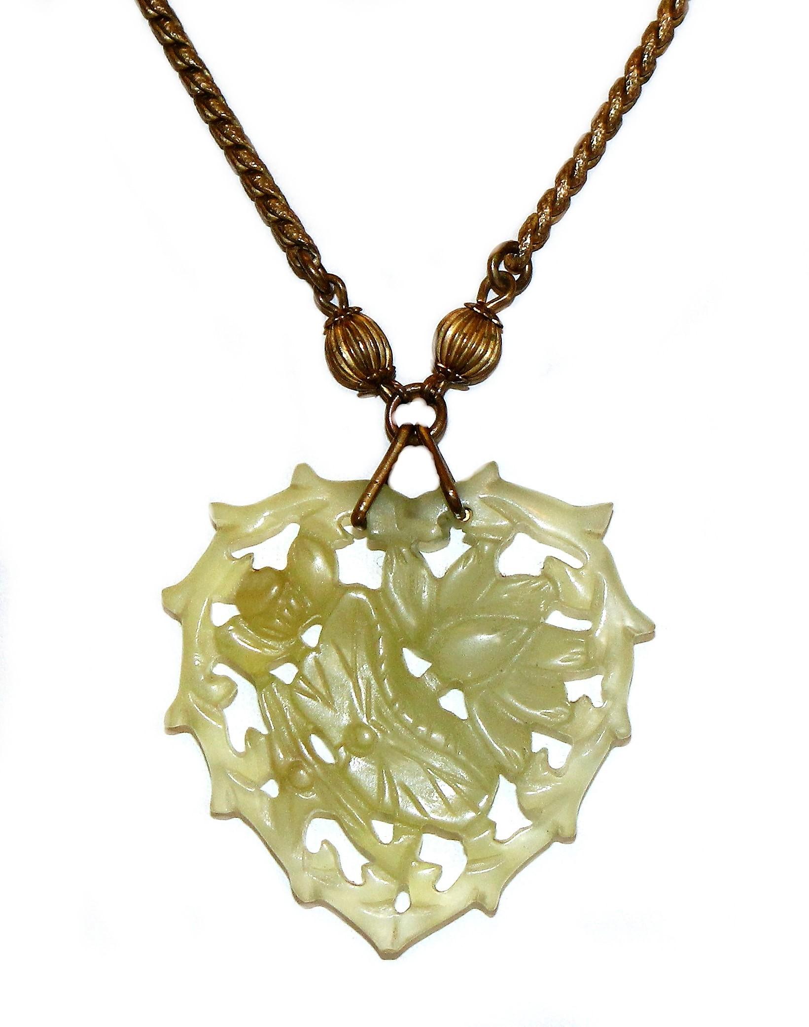 Circa 1970s Miriam Haskell long gold tone necklace with a pale green molded glass heart decorated with a water lily and butterfly motif.  The necklace is embellished with beads of jade-green glass and brass.  It measures 30