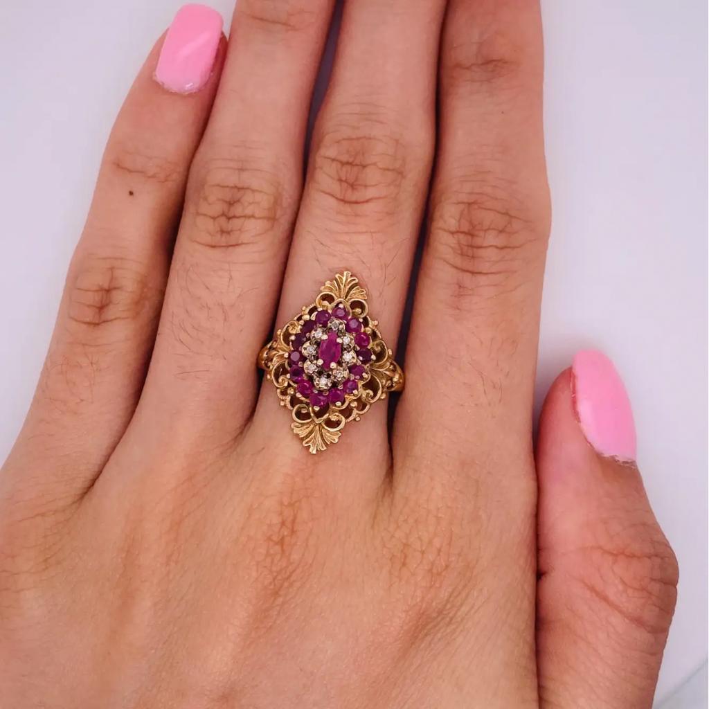 Luxurious openwork filigree and flourishes create the backdrop for this gorgeous ruby and diamond cluster ring. The ring design centers around a lovely richly red marquise shape ruby. The rest of the ring top echoes this marquise shape with tiers of