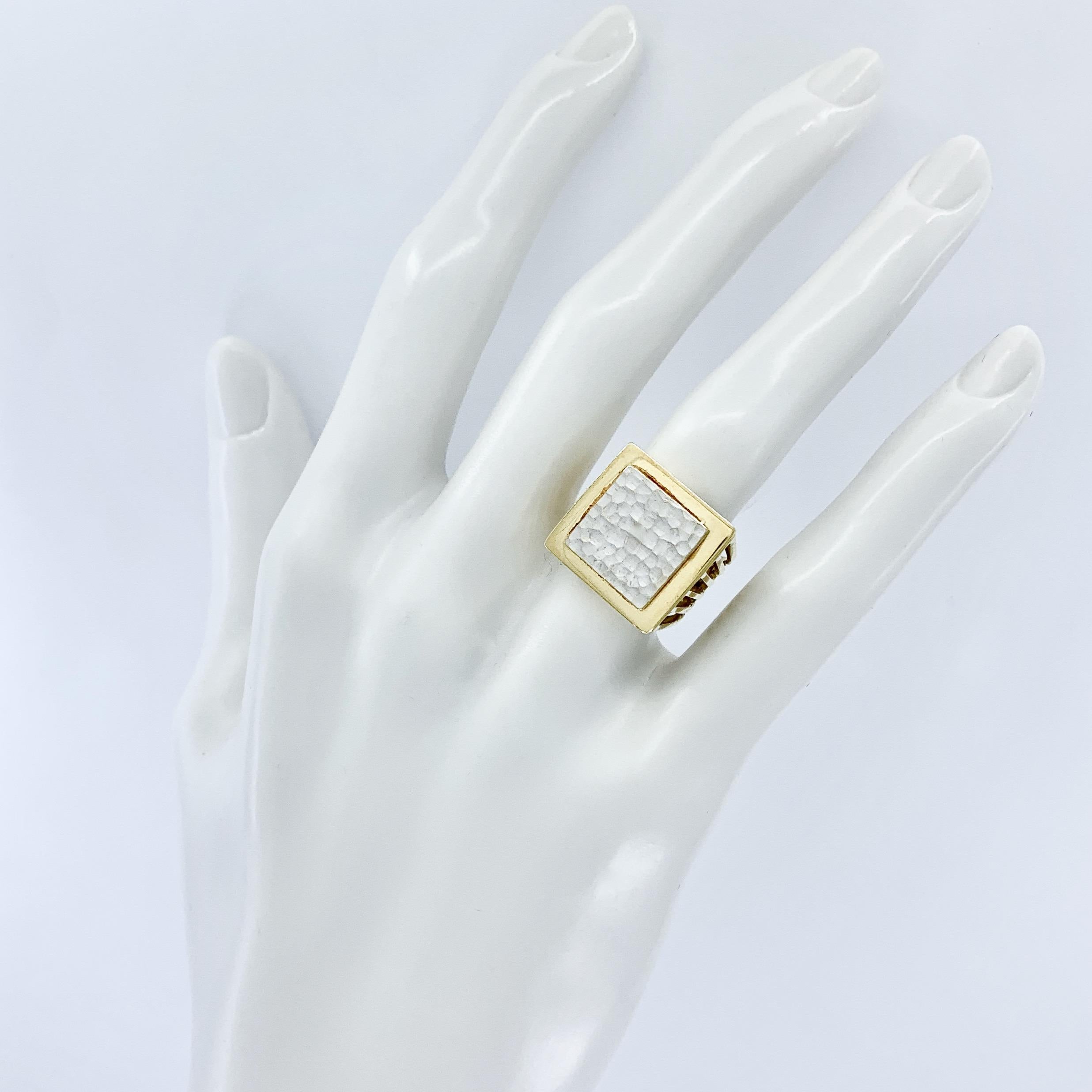 This strong, architectural ring features a square, engraveable slab of hammered white gold set in a polished yellow gold D-shaped ring with wide, slatted sides tapering to a solid back.  Great contrast in colors and textures, all in 18 karat