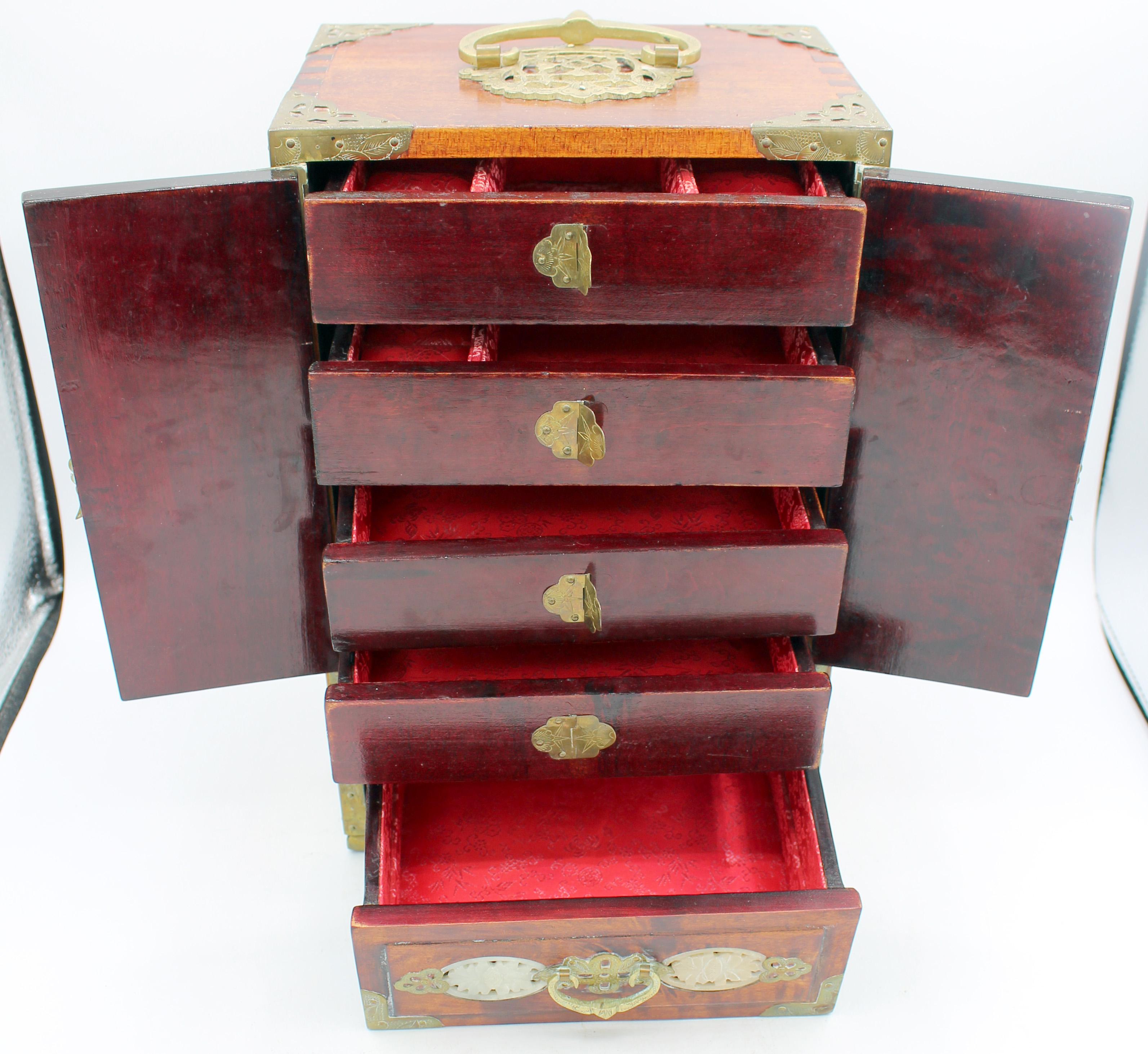 Circa 1980s Chinese table top jewelry chest or cabinet. Doors revealing 4-silk lined drawers above a large lined drawer. The highly figured native wood is inlaid with carved jade panels & bound in engraved brass. Retains Peoples Republic of China
