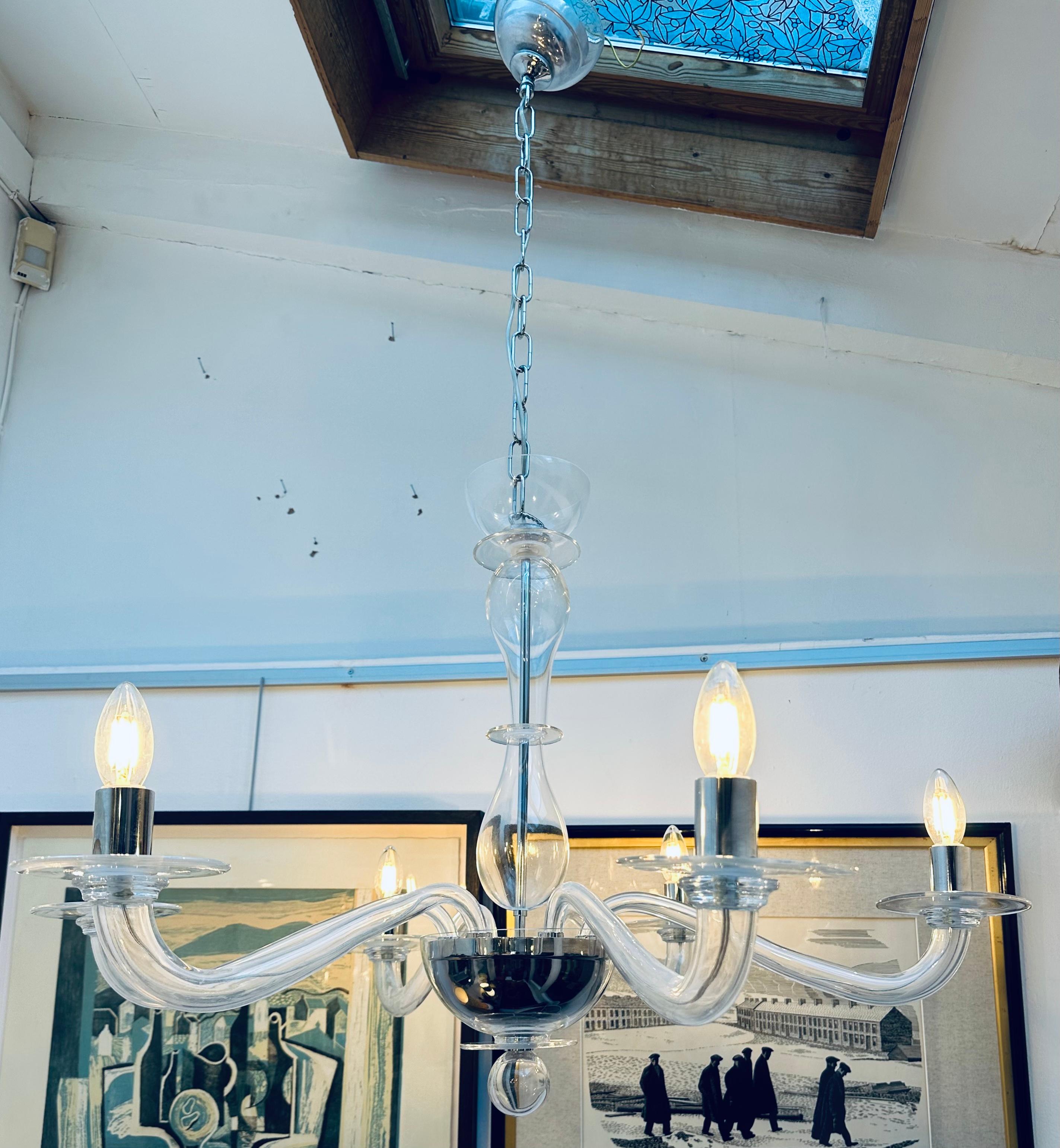 Circa 1990s Italian Murano transparent six-arm clear glass modernist chandelier by manufacturer Sylcom.  The six modernist chrome tubular bulb-holders each require a single E14 screw-in bulb.  A flat circular disc sits below each one to create the