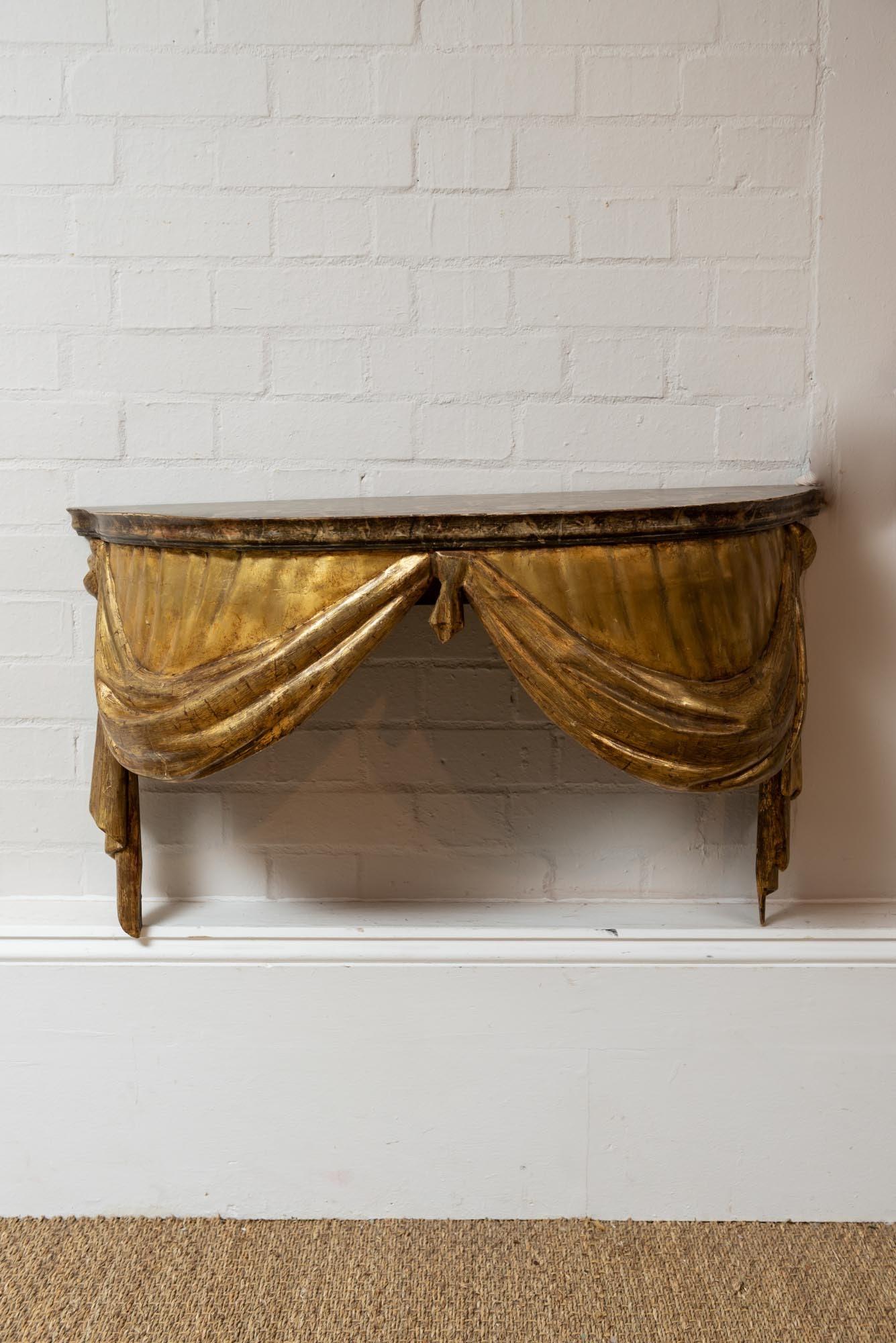 A highly decorative and unusual console table from the late 19th century. The console features a faux marble painted top with a beautifully crafted gilded and painted draped and swagged front. The wall hanging console fixes directly onto the wall.