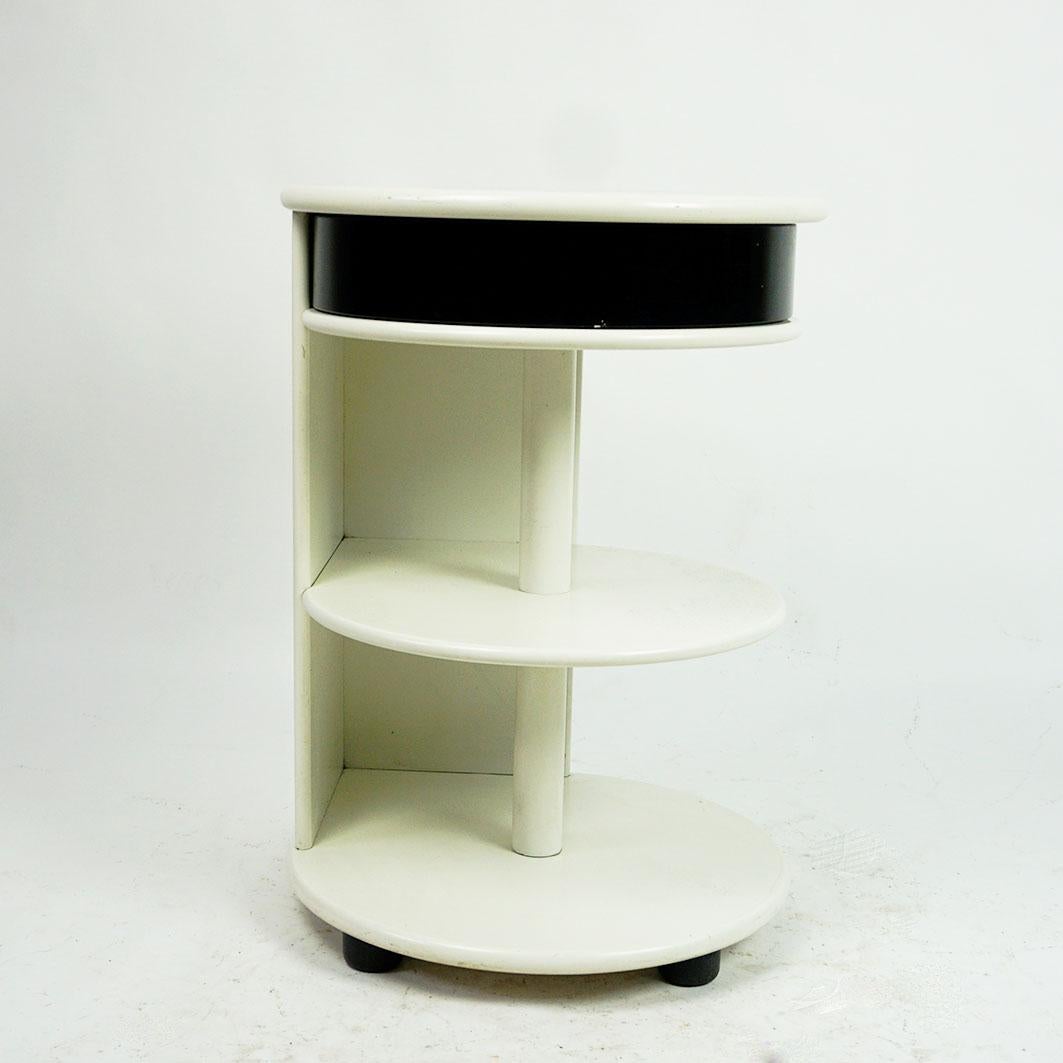 This outstanding white and black lacquered postmodern circular side table or nightstand was designed and manufactured in Italy 1980s. 
It features a white lacquered body with one black lacquered drawer and black lacquered legs. It is in very nice