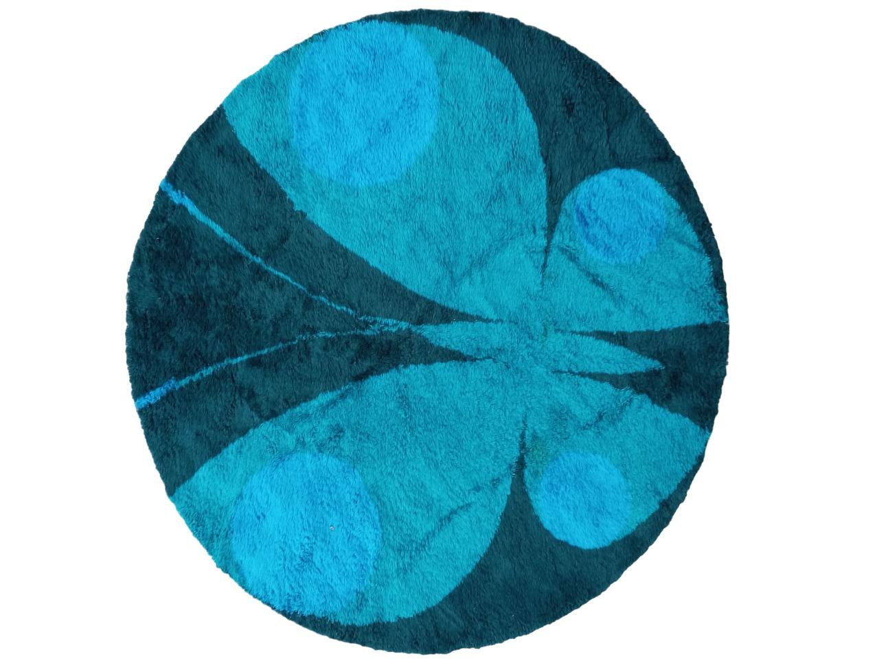 This carpet is a magnificent circular specimen with an impressive diameter of 275 centimeters. Its base is an intense and enveloping shade of blue, creating a pleasant sensation of depth and serenity. At the center of the carpet, stands out a large
