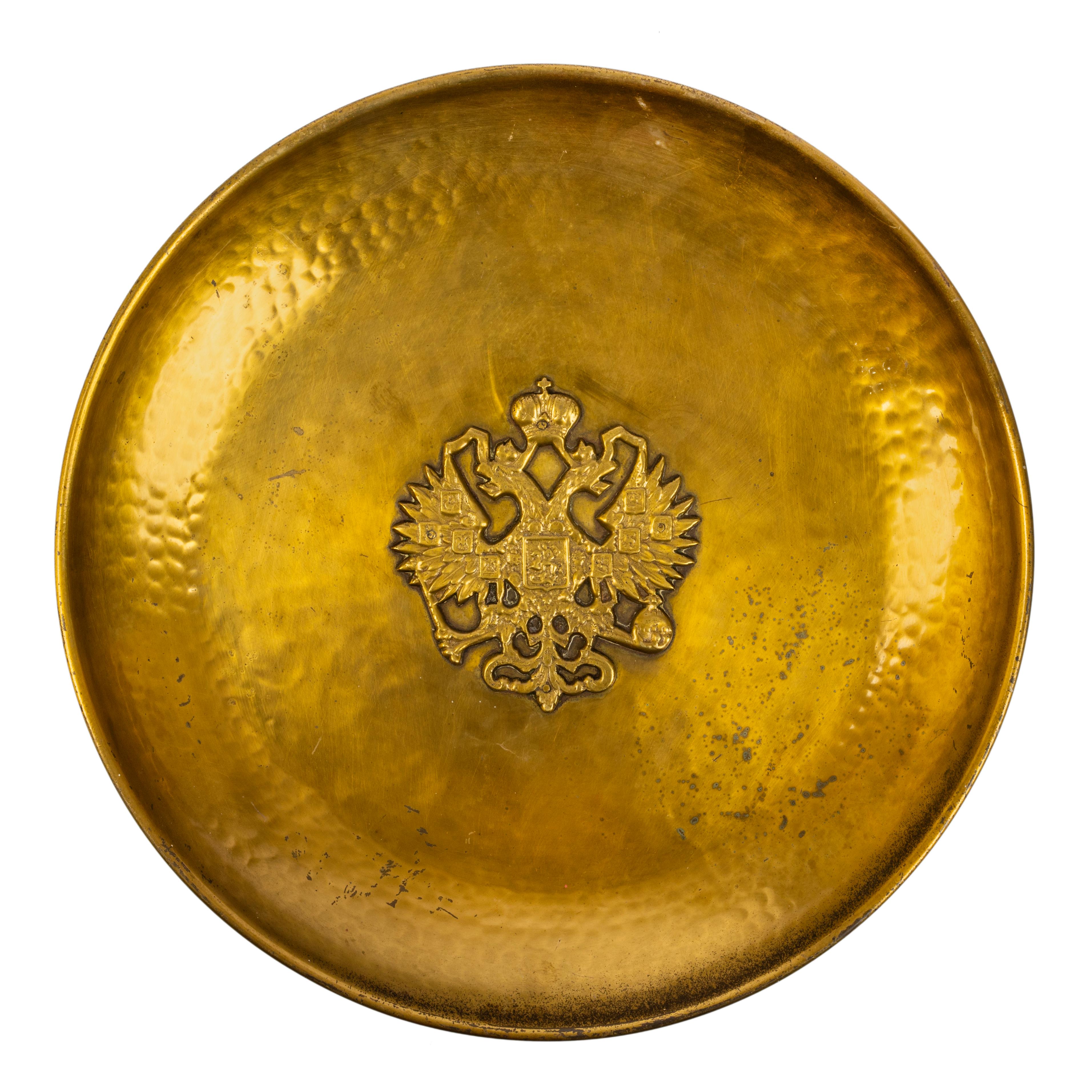 In the Russian style, a large circular brass serving plate with everted rim, of overall hand hammered design, the center applied with a Russian double headed Romanov eagle holding orb and scepter, enclosing the shield of St. George Slaying the
