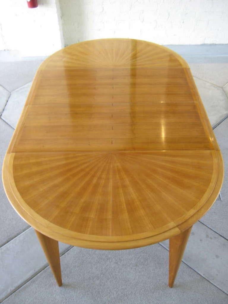 A circular French cherrywood expandable dining table with two leaves, attributed to noted French designer Baptistin Spade, circa 1940s.
The top of the table is composed of choice veneers that create a radiating, sunburst pattern. Each of the leaves