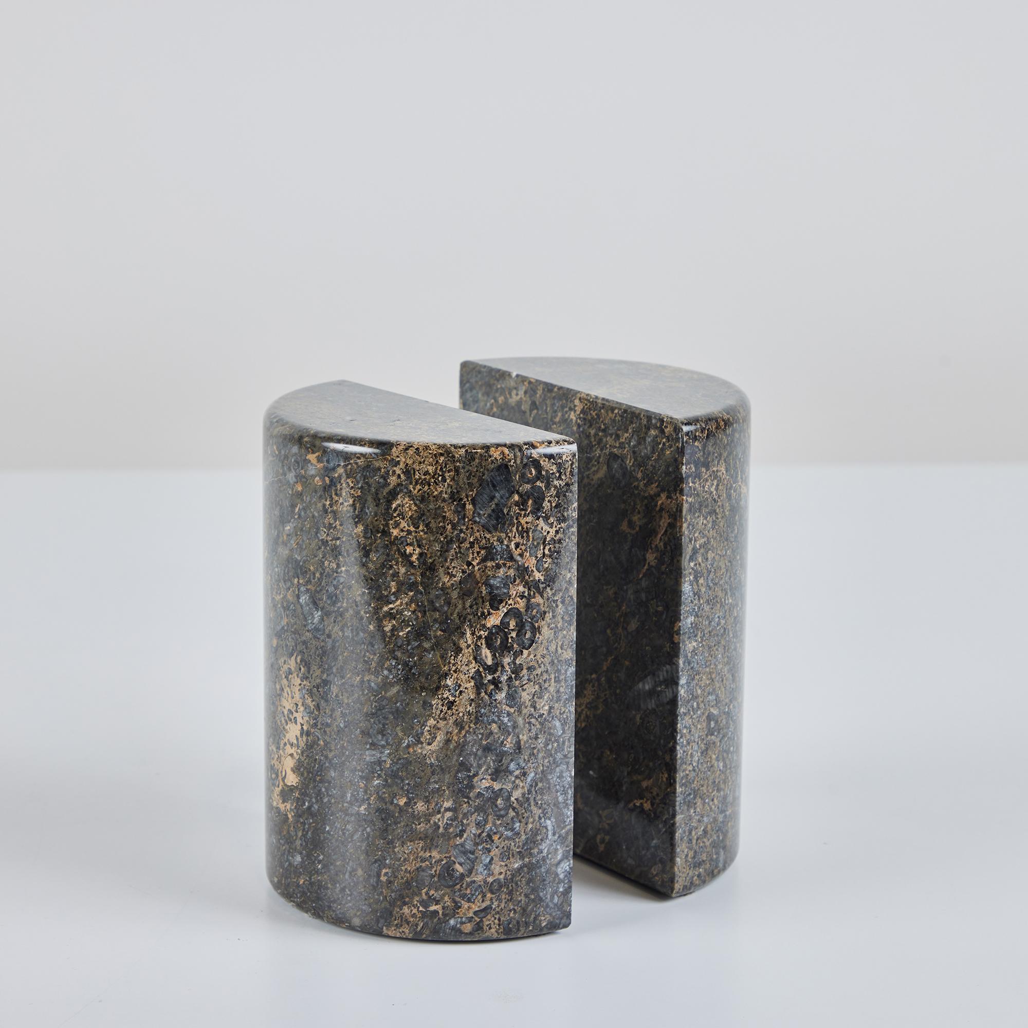 Pair of marble bookends feature a half circle shape with smooth rounded edges. When placed together they form an elongated circle. The stone showcases varying speckled tones of dark gray brown and black with tan and cream veining throughout the