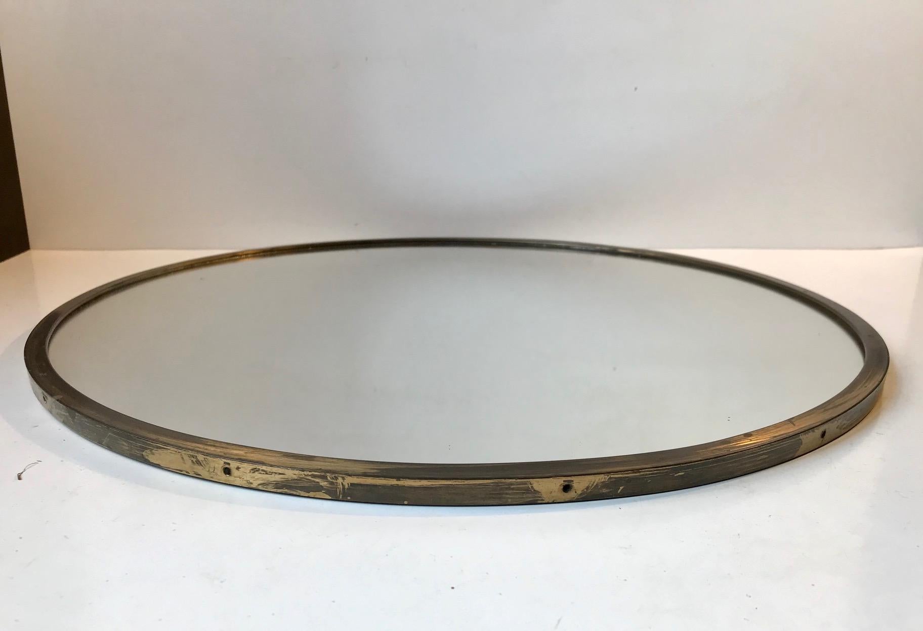 A round wall mirror in a patinated solid brass frame. Stylistically very funktionalist, simple and plain. Its just a mirror and it was made in Italy during the 1950s or perhaps a bit earlier. Measurements: D: 43.5 cm, Dept: 1 cm.
