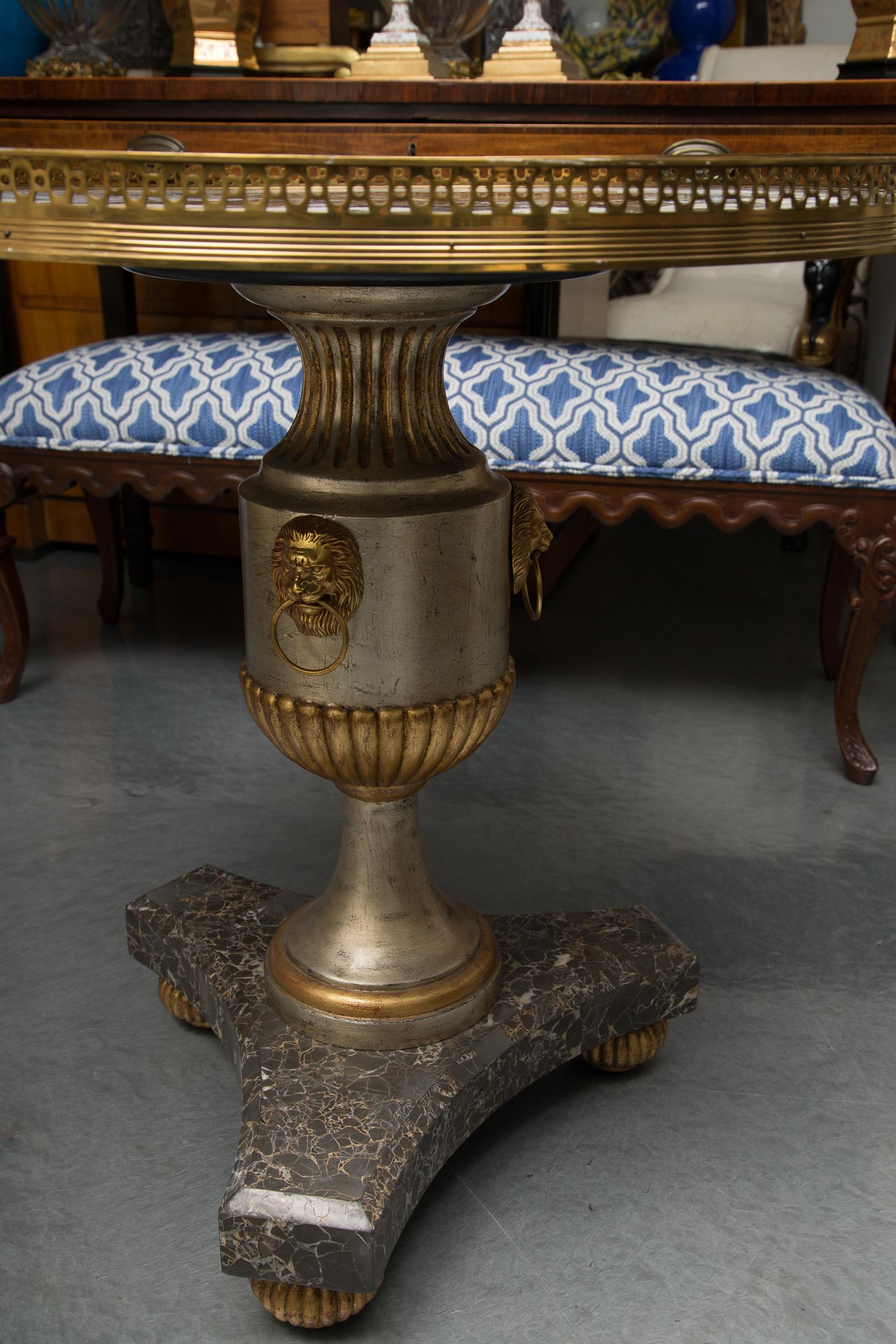 This is a decorative circular table with an inlaid marble top framed by a pierced brass gallery and supported by a silver-gilt baluster pedestal situated on a tripartite marble plinth supported by gilt ribbed bun feet, circa 1950.
