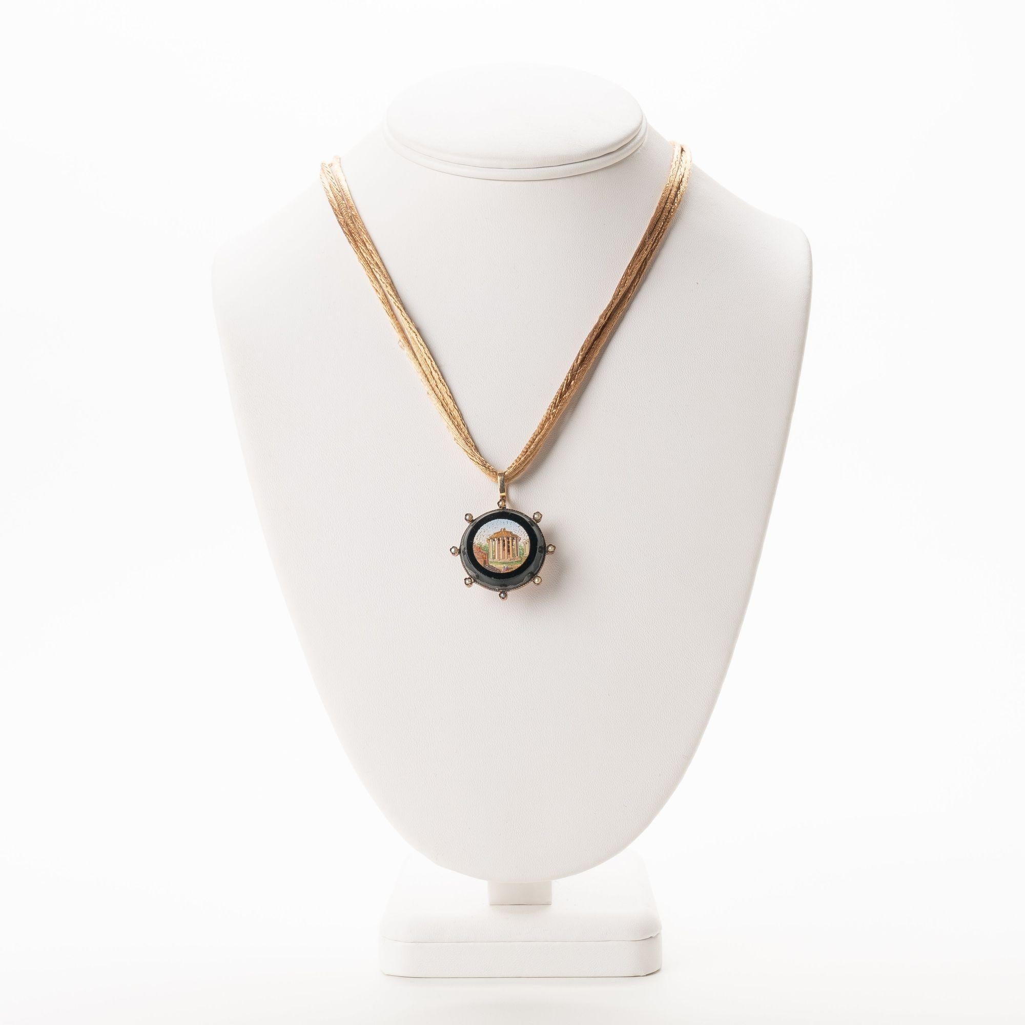 Circular micro mosaic pin pendant centers on the Temple of Vesta in the Roman forum. The micro mosaic pin is set in black glass, mounted in a gold bezel with eight radial mounted pearls, and fitted for use as a necklace on silk cords with 14k gold