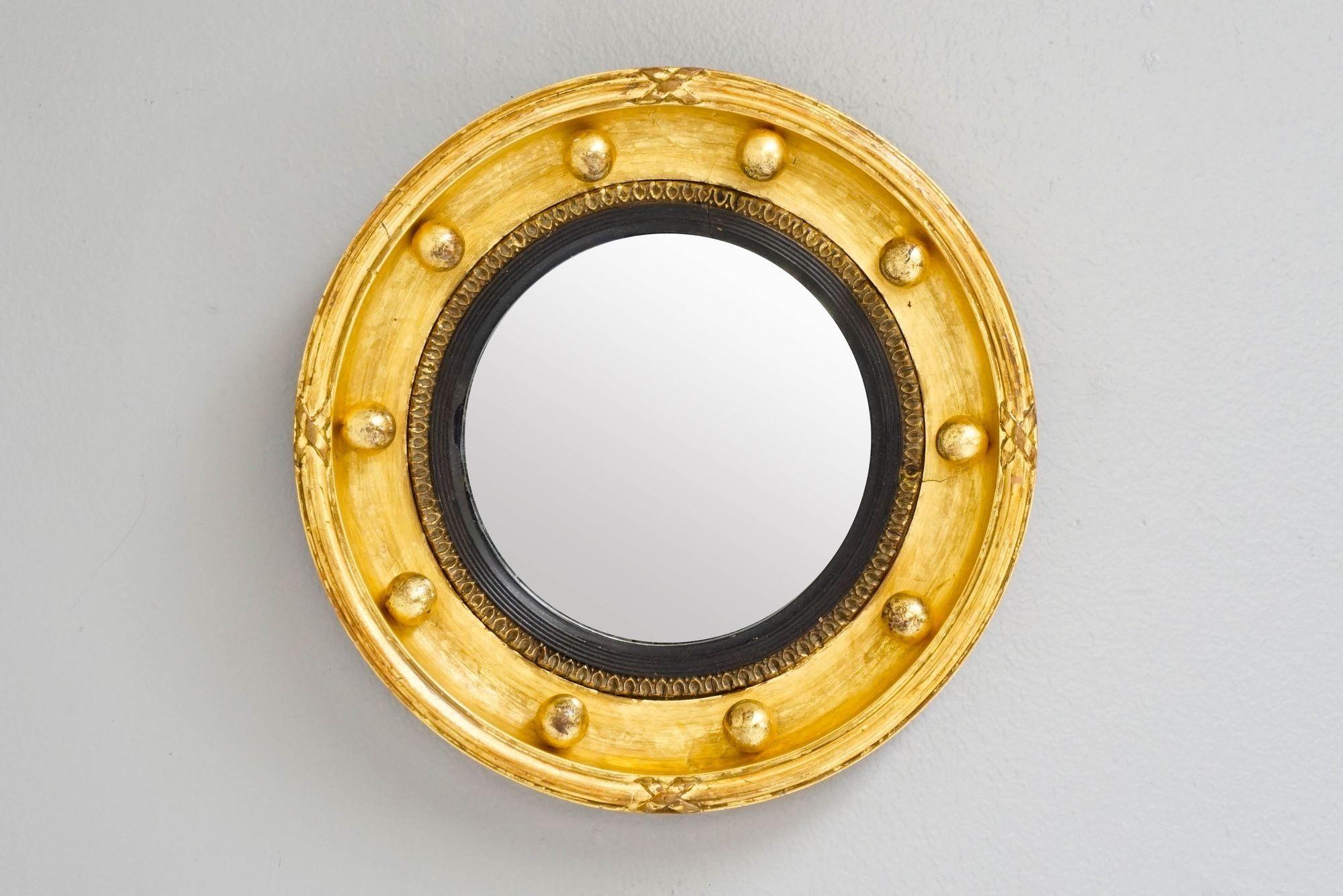 Espejo circular dorado con marco de resbalón negro y decoración de cintas.