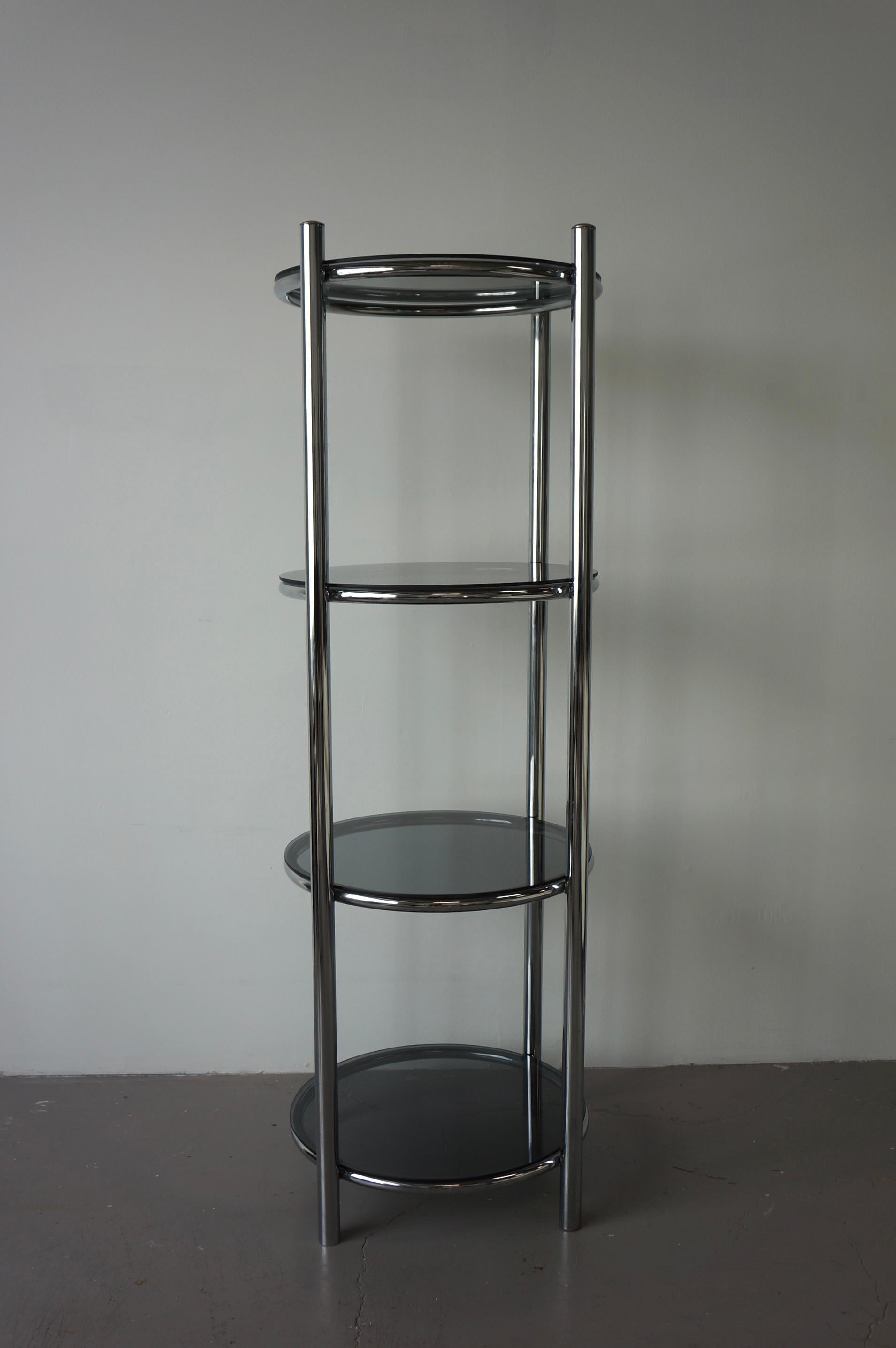 Circular chrome shelf with smoked glass shelving. This piece is a classic reminiscent of mid century modern design. It was made in the late 1960s. The chrome shelf is tubular with thick rounded frame featuring smoked glass shelving. The four legs of