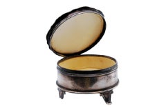 Circular silver jewelry box with engraved plant motifs and raised feet
