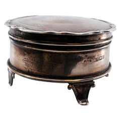 Circular silver jewelry box with engraved plant motifs and raised feet