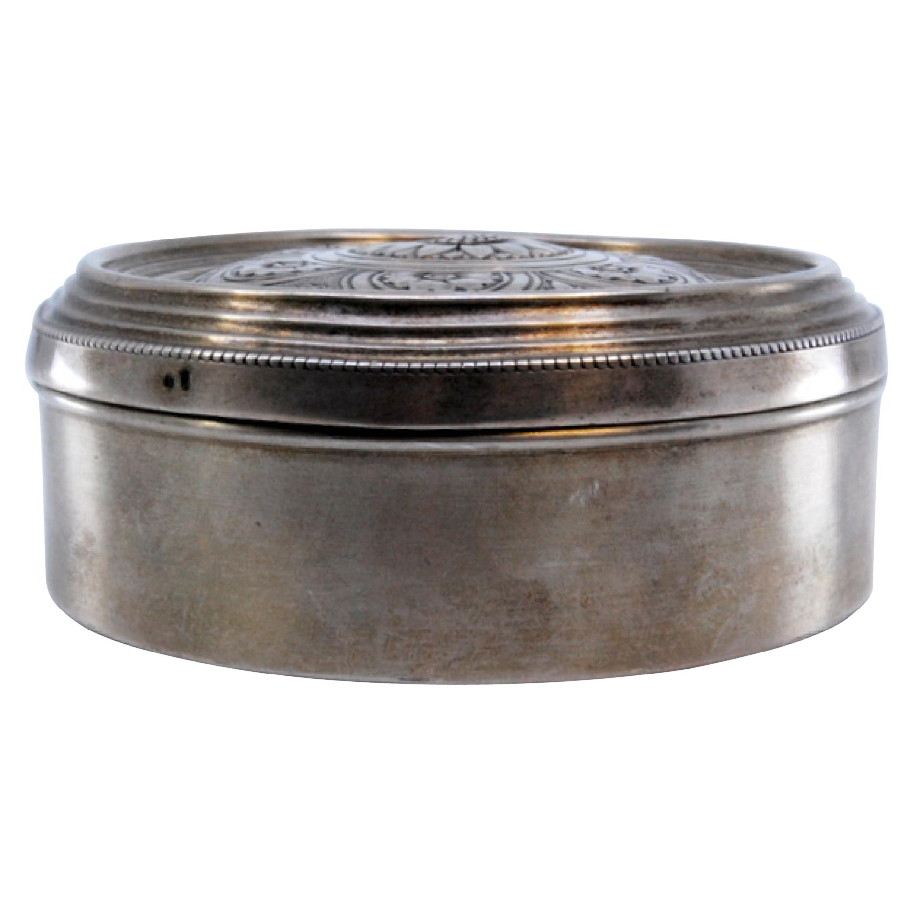 Circular silver jewelry box with floral motifs engraved on the hinged lid