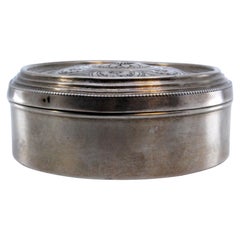Circular silver jewelry box with floral motifs engraved on the hinged lid