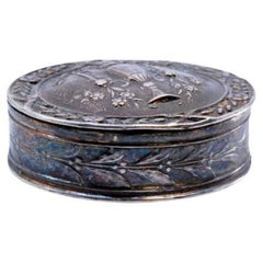 Circular silver pill box decorated with floral reliefs on the hinged lid