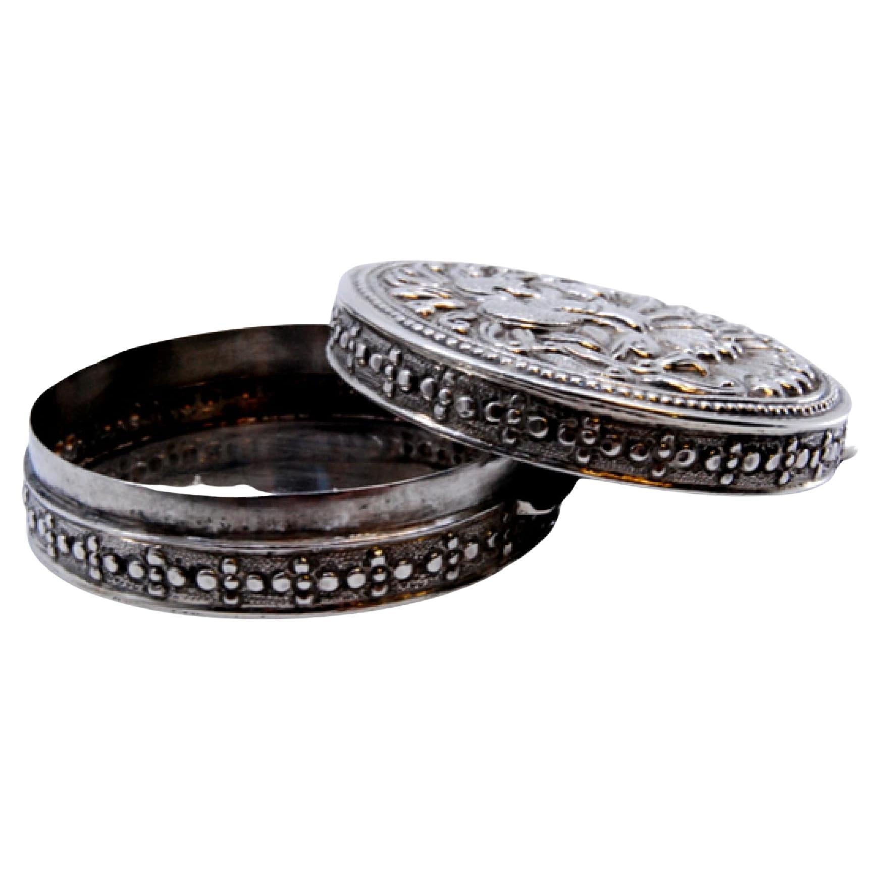 Circular silver pill box with a pair of peacocks embossed on the removable lid