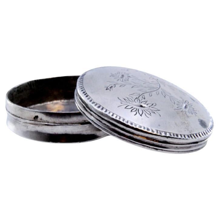 Circular silver pill box with floral motifs engraved on the removable lid