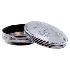 Circular silver pill box with floral motifs engraved on the removable lid