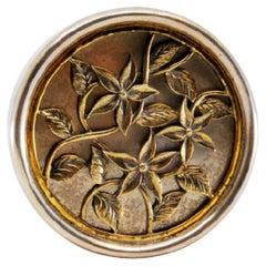 Circular silver pill box with gold floral motifs embossed on the removable lid