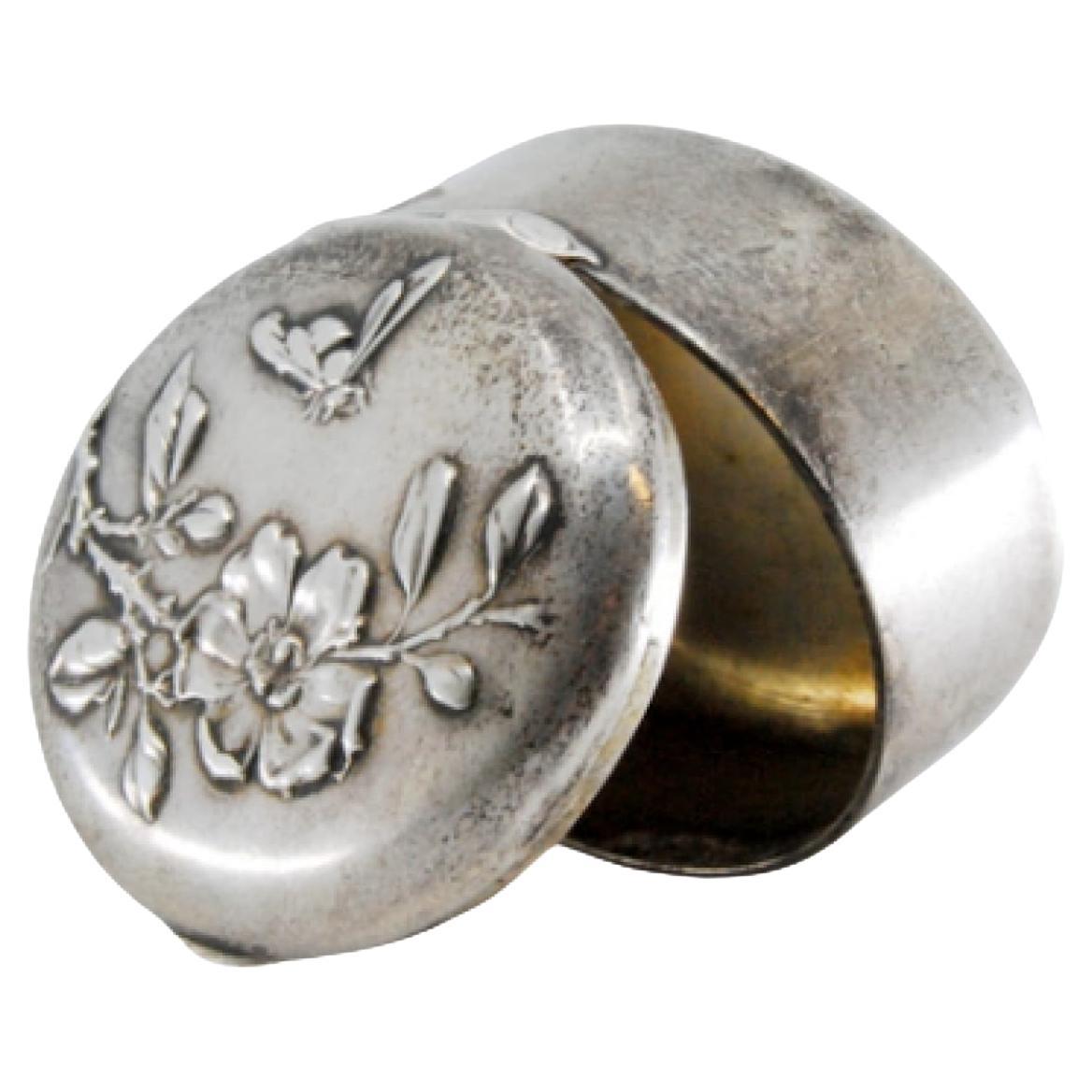 Circular silver pill box with raised floral motifs on the hinged lid
