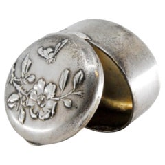Circular silver pill box with raised floral motifs on the hinged lid