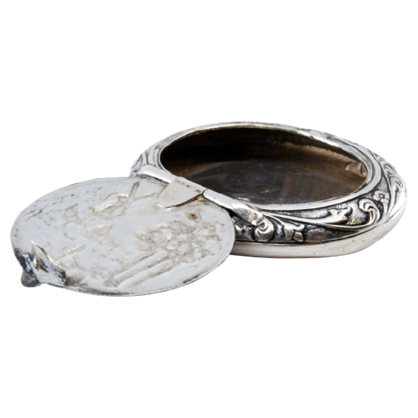 Circular silver pill box with reliefs and a hinged lid