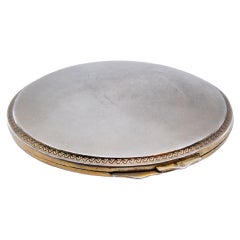 Circular silver toiletry box w/ a frieze around the edge
a gold mirror inside