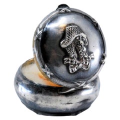 Circular silver toiletry box with mirror inside and relief on the lid