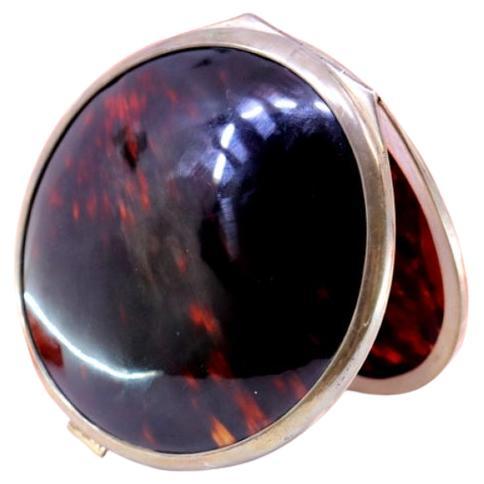 Circular tortoiseshell box with silver trim, hinged lid and spring closure