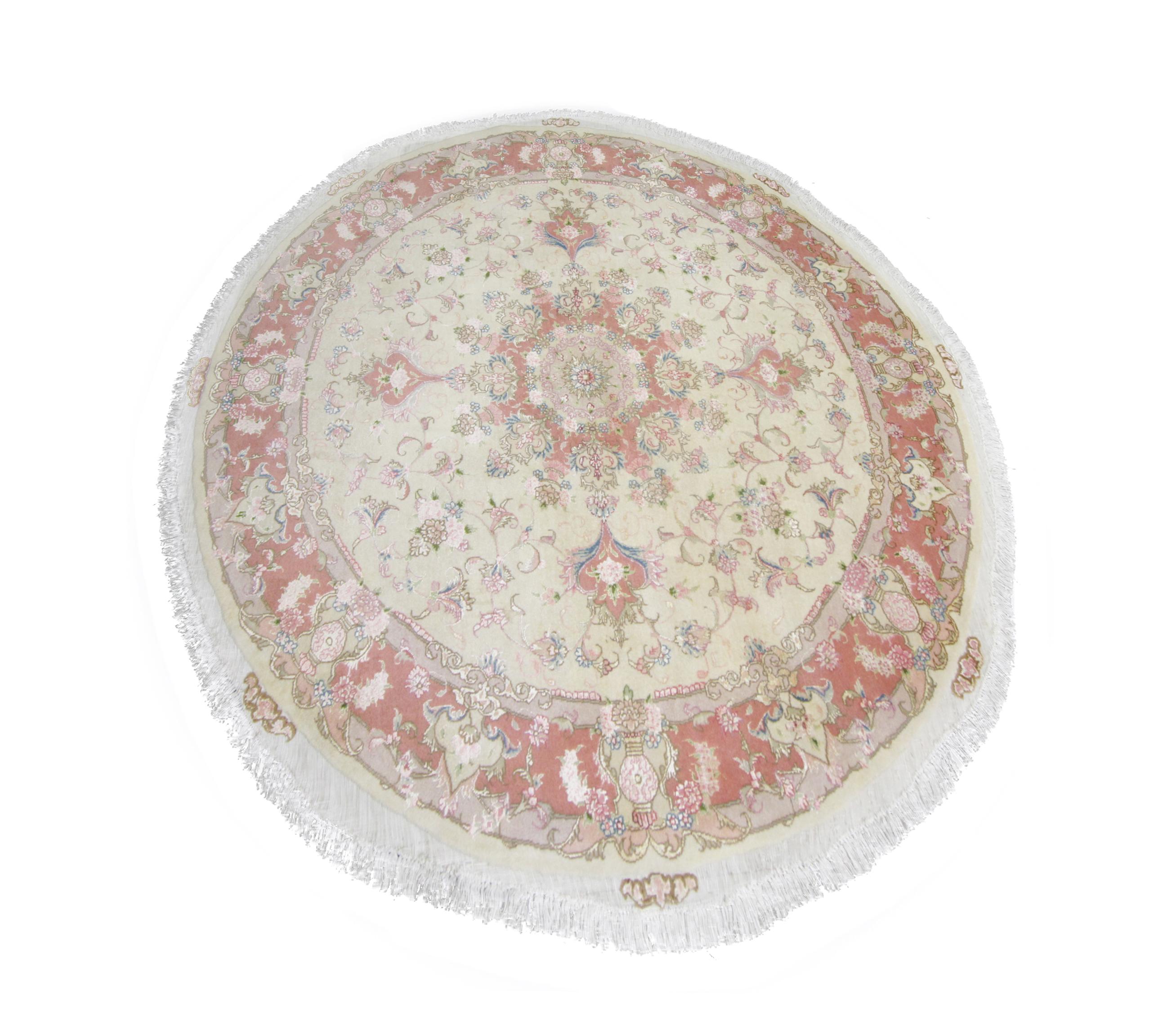 This small circular wool rug was woven in Turkey in the 2000s with fine organic silk and wool materials. The design features a cream background with pink, ivory, blue, and green accents that make up the intricate symmetrical medallion design. This