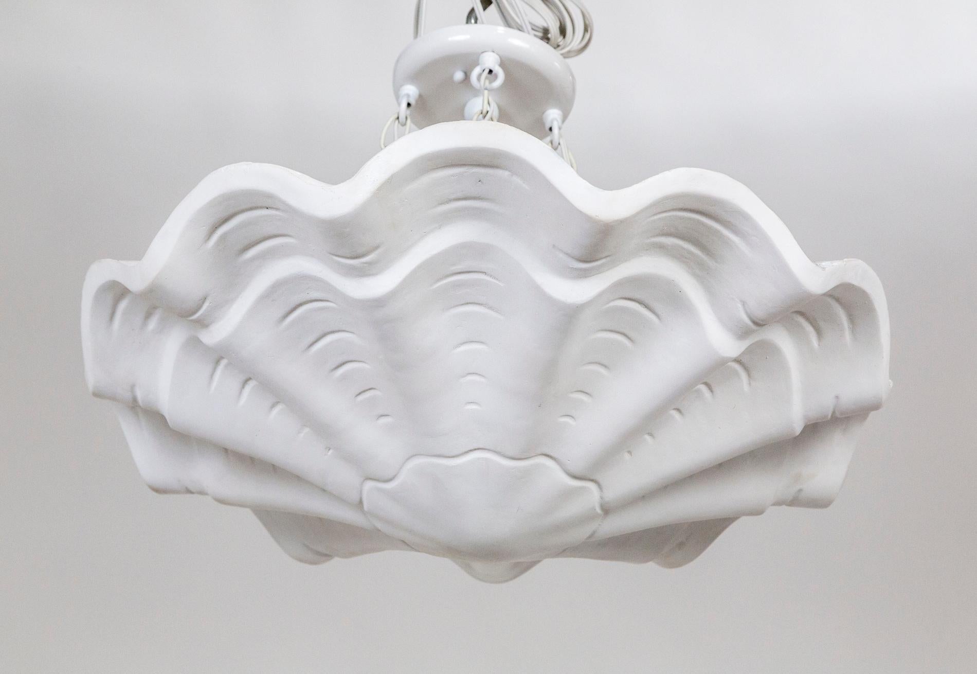 A plaster pendant in an undulating shell shape, with scalloped edges and imprinted lines accentuating the form. A newer take on Francis Elkins's 1940's plaster plafonnier. Hanging by four white chains; with 3 medium base ceramic sockets.