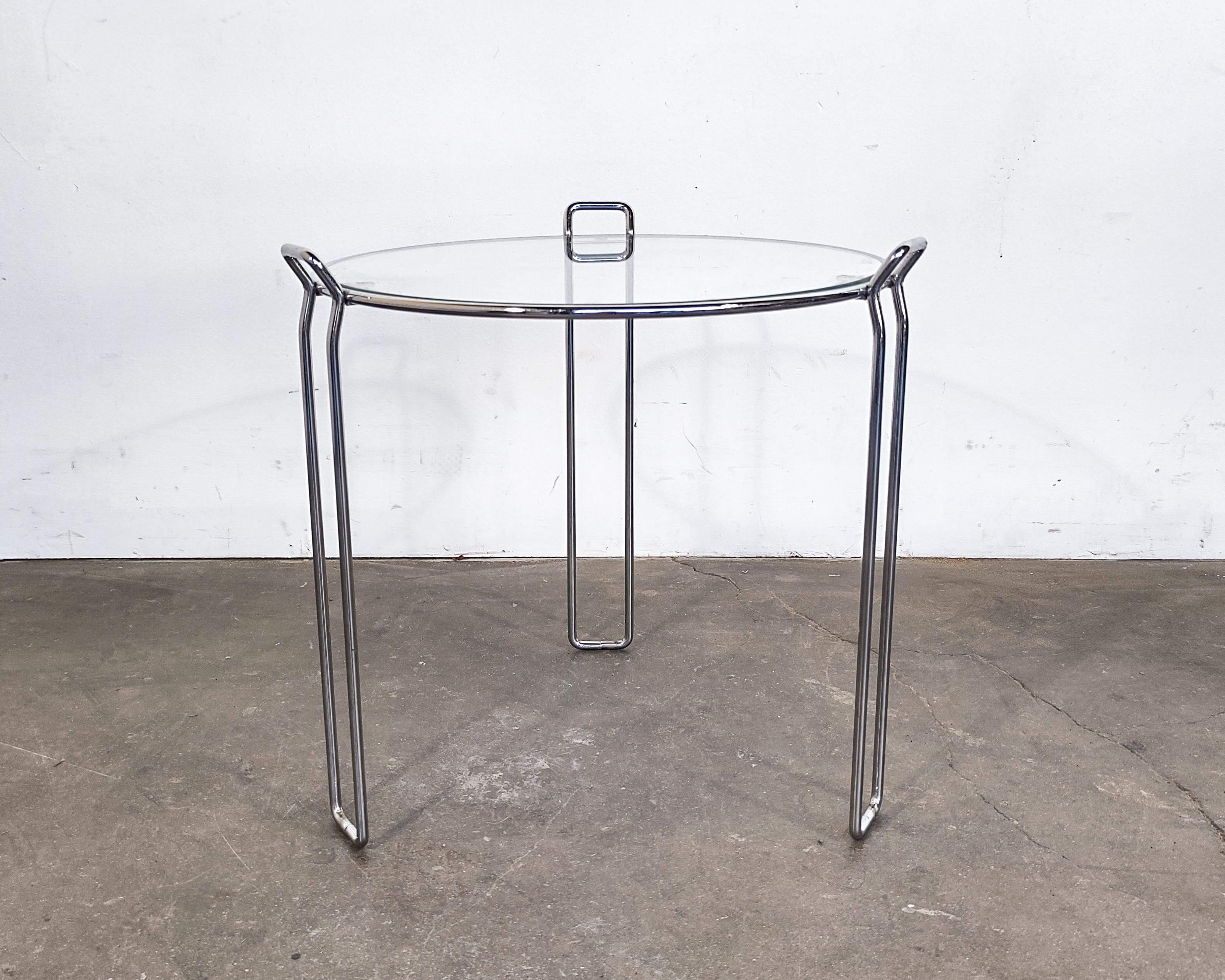 Minimalist wire frame chrome side table with glass top. Tripod base with legs extending into handles. Chrome is mirrored and has very slight surface patina in some areas. Excellent vintage condition, some scratches to glass, no chips.

15.75
