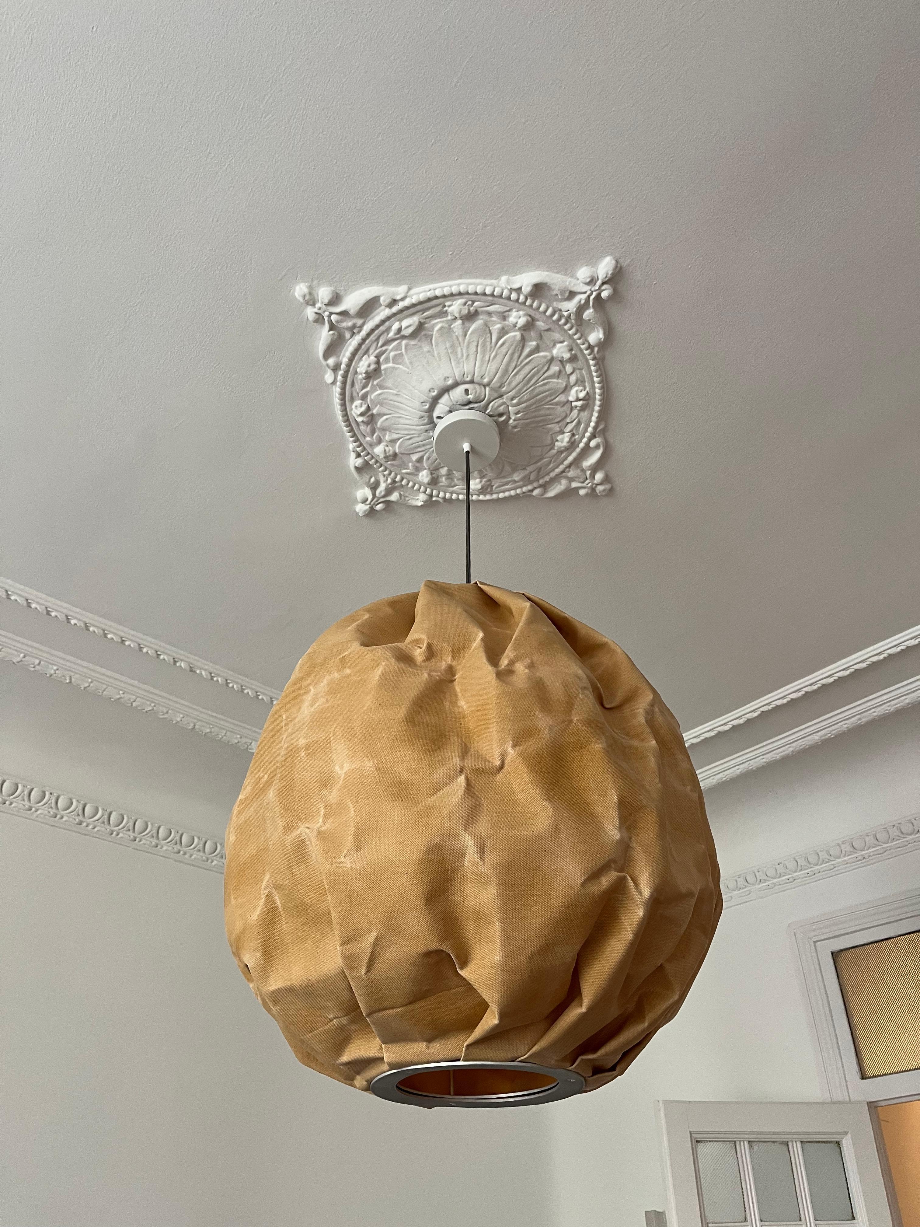 Beeswax est une sculpture lumineuse suspendue de Pablo Bolumar. Fabriqué en toile cirée à la cire d'abeille, l'abat-jour génère une lumière chaude et texturée, accentuant les plis et les rides de la fabrication. L'œuvre d'art suspendue porte un