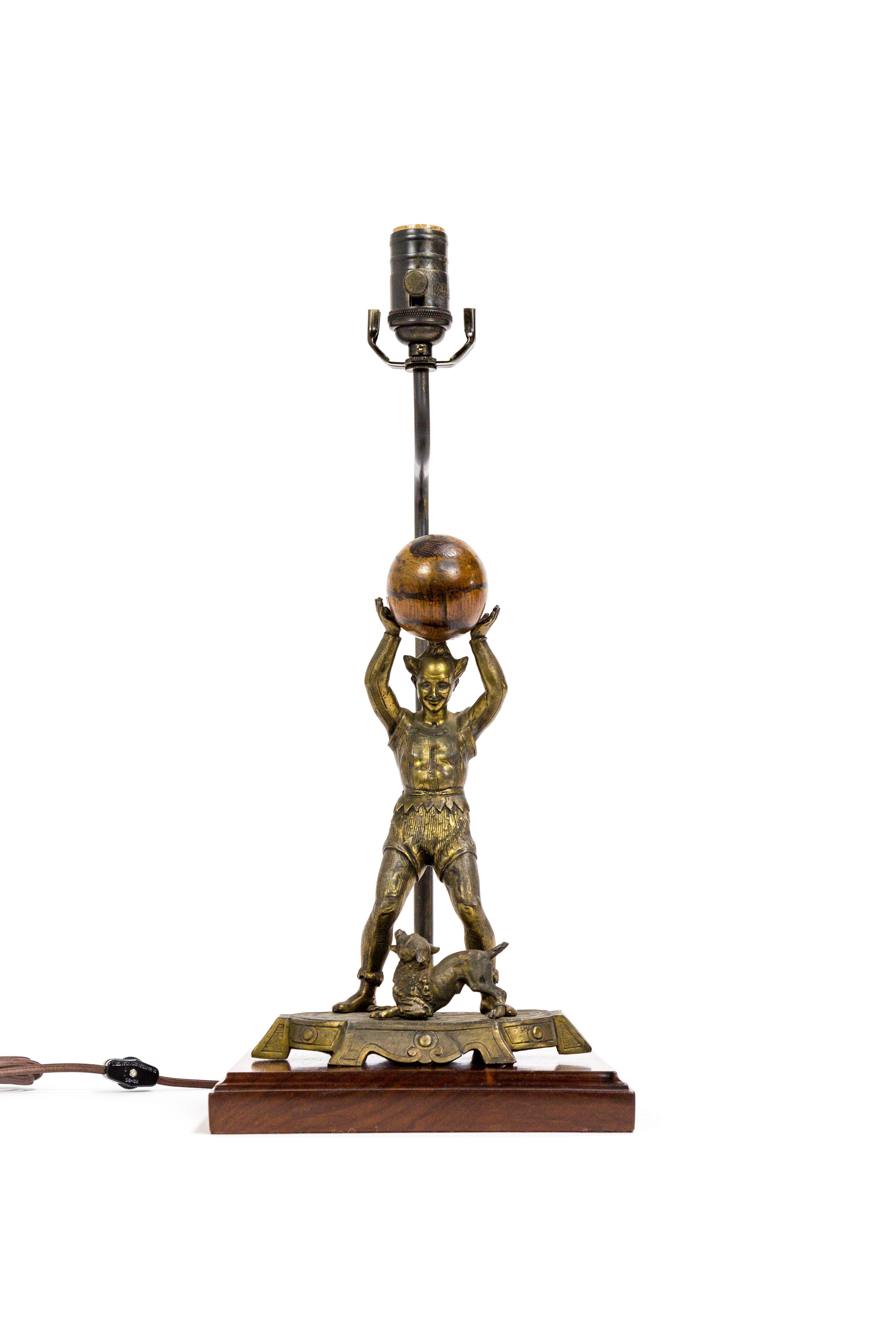 A lamp made with an exceptional sculpture of a circus performer holding a wooden ball with marvellous grain, with a dog at his feet. (Spelter with brass patina). The piece was made in France in the 1880s; now complimented by a walnut base and