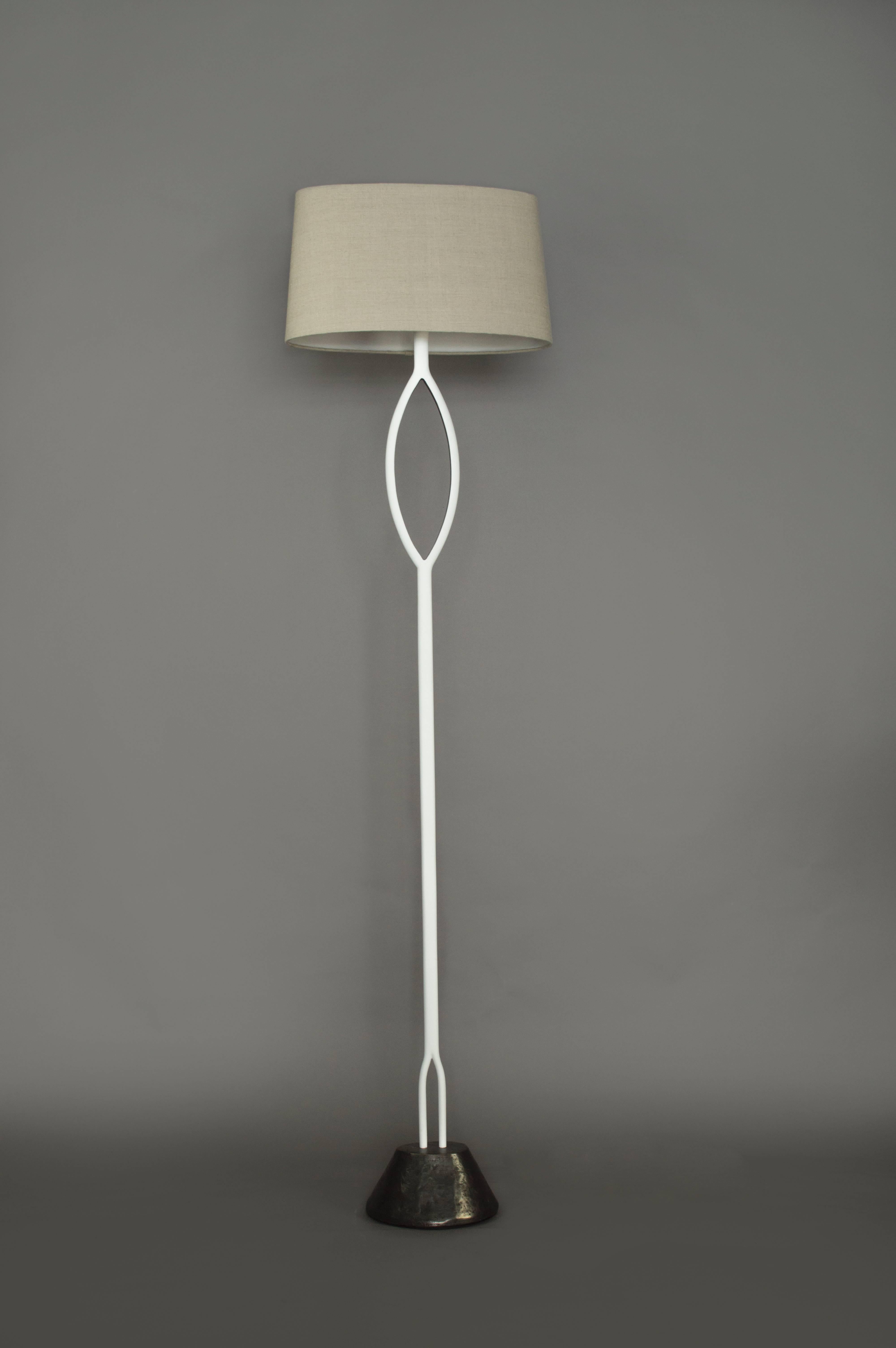A slender floor lamp handcrafted in plaster. A cast bronze base and a linen shade complete the light. The light has one medium based bulb with a three-way socket.