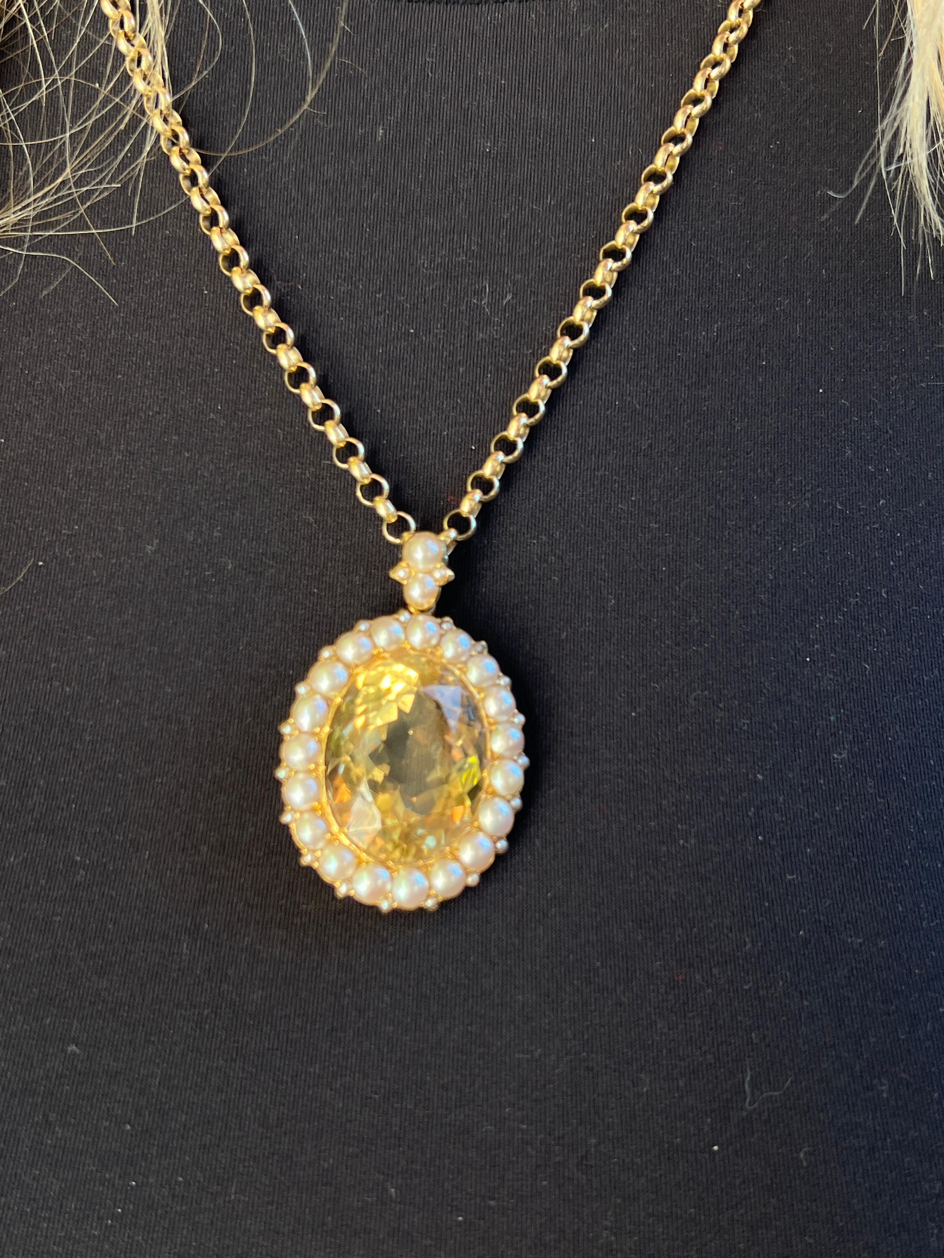 Un grande Citrino naturale di colore giallo chiaro e taglio ovale, incastonato in un bordo di mezze perle e accentuato da perle di seme, con una catena con perle incastonate. L'abbellimento a reticolo traforato della metalleria sul retro conferisce