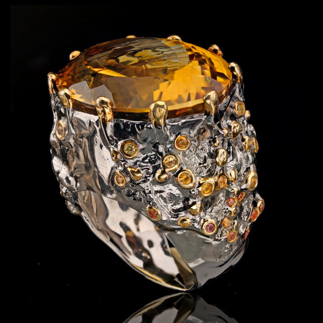 This massive, flawless oval-cut amber-hued citrine fills a fantastically unique hand-tooled rhodium plated sterling silver prong setting featuring a plethora of accenting rare orange and yellow sapphires and ornamented with gold leaf.

We will