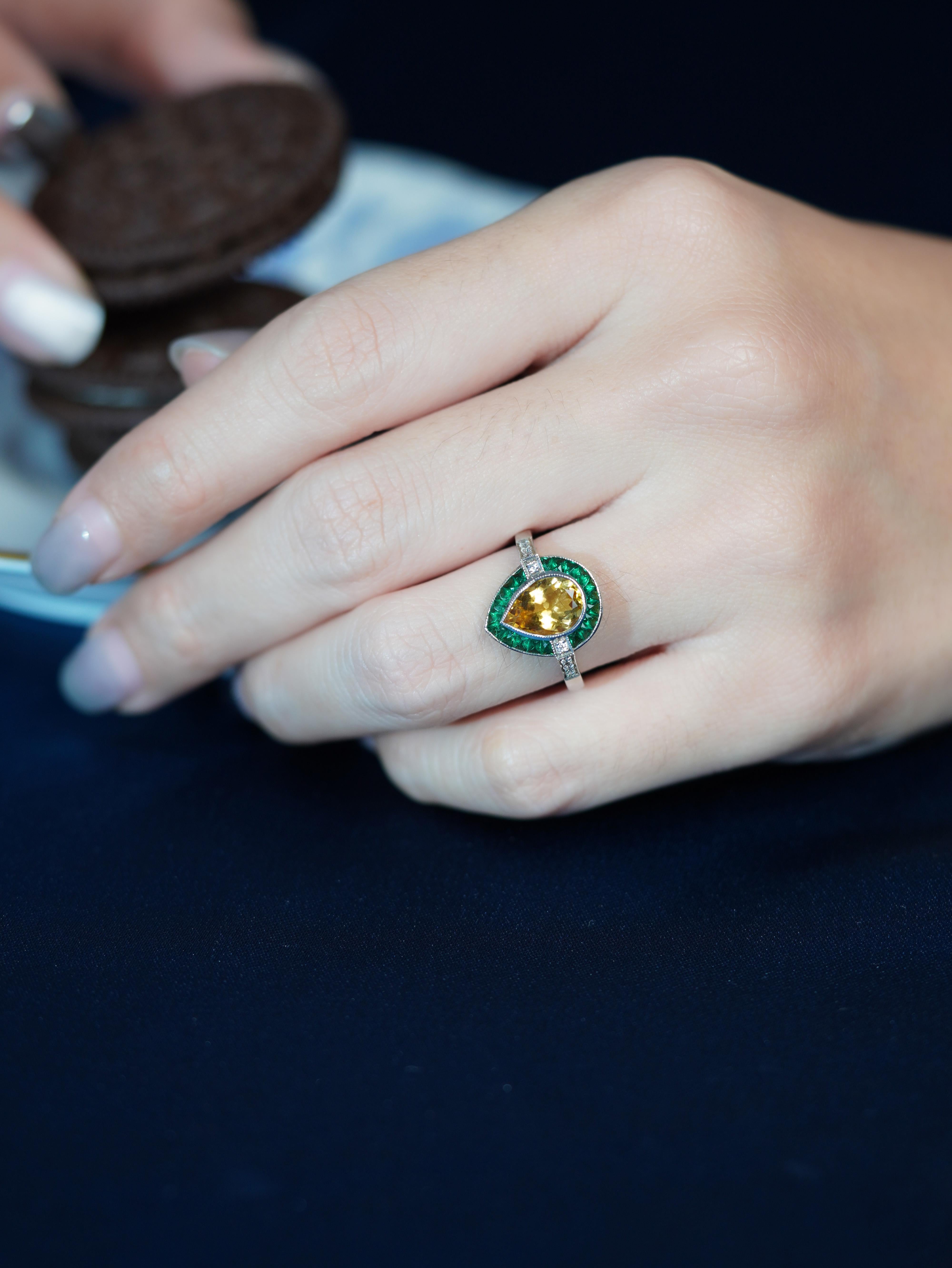 Questo anello di fidanzamento unico di ispirazione Art Déco ha come centro un vibrante citrino a forma di pera che irradia calore ed eleganza. È splendidamente incorniciato da smeraldi verdi taglio francese, che creano un contrasto sorprendente. Le
