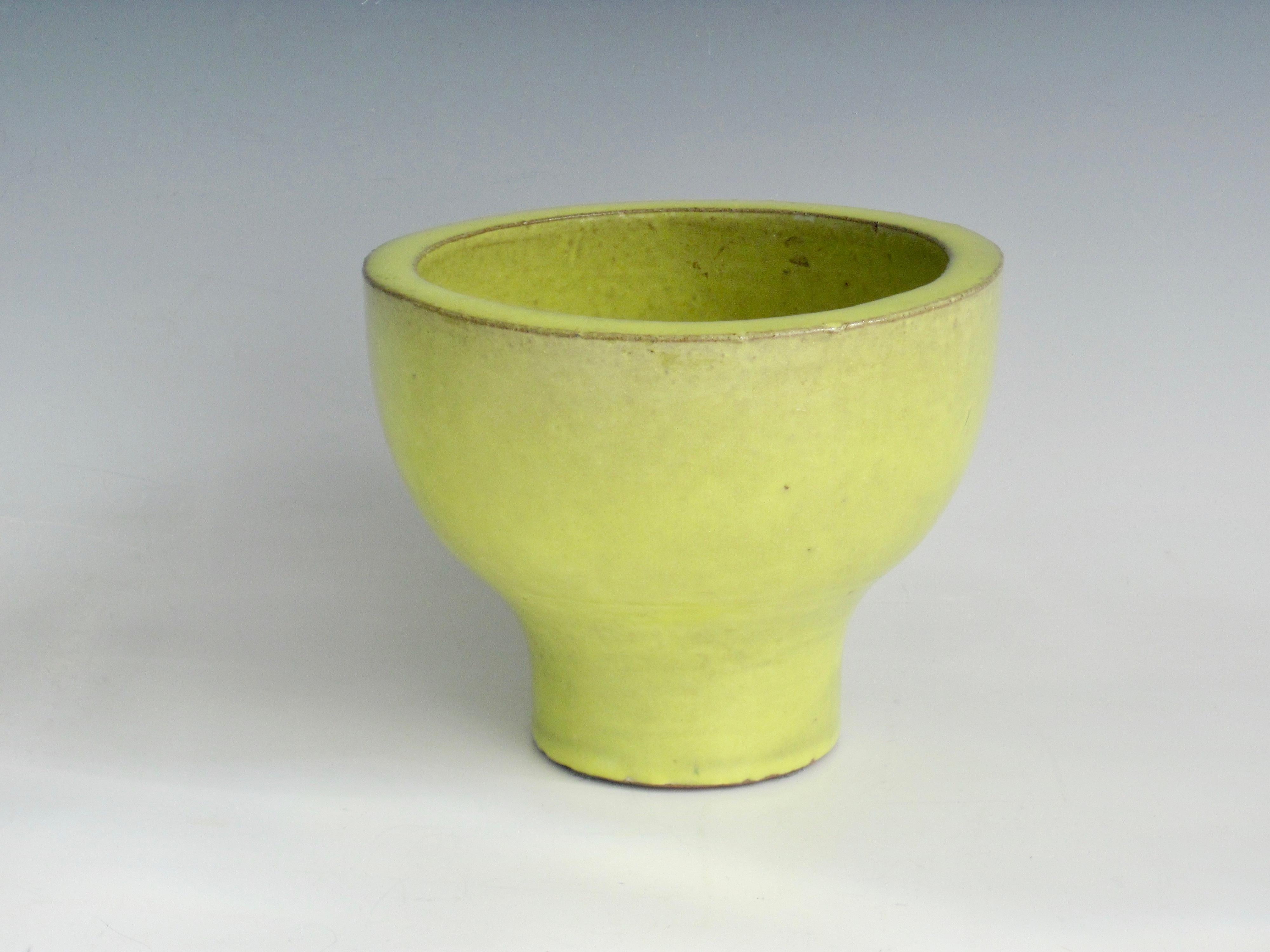 Thick terra cotta pedestal planter pot or bowl in glossy citrine yellow. Rim varies in height and natural flecks in the glaze throughout give a rustic feel. The vibrant color makes it pop.