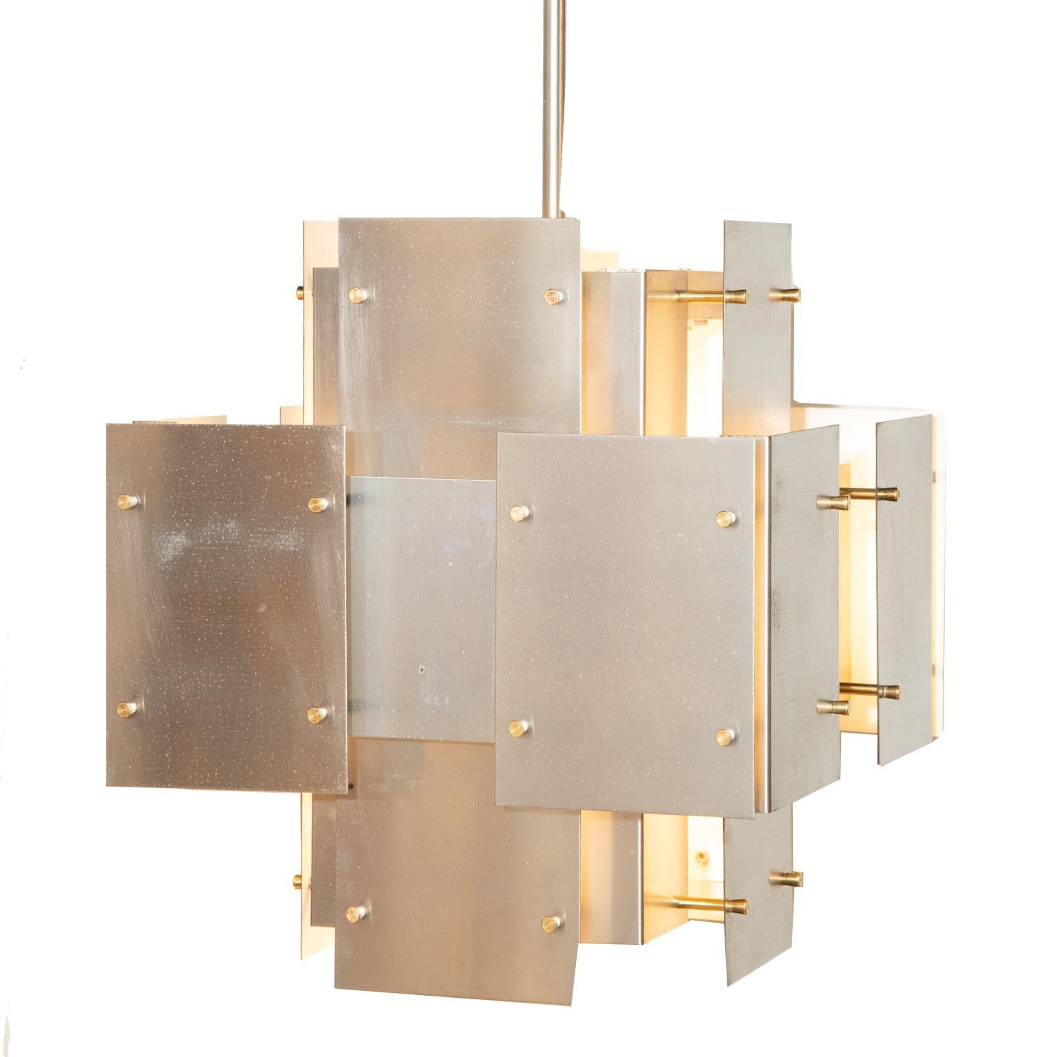 Questo lampadario architettonico, fresco e sofisticato, con pannelli geometrici in acciaio spazzolato a incastro e accessori in ottone, è opera del pioniere dell'illuminazione Robert Sonneman, americano degli anni Settanta.  Questo lampadario è di